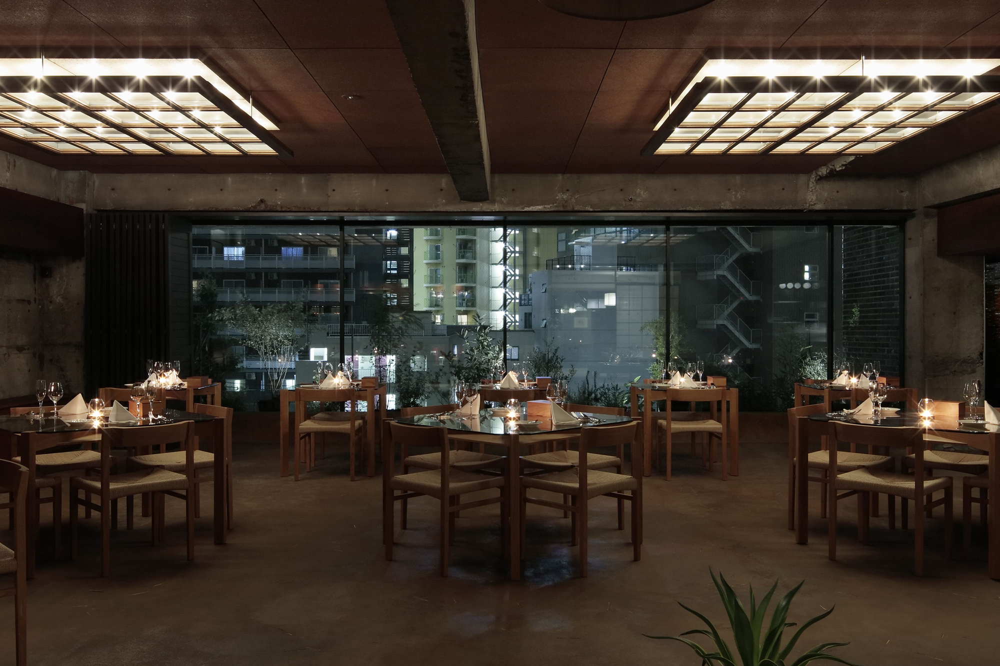 Dining room with wooden tables set for service beneath illuminated ceiling panels at night