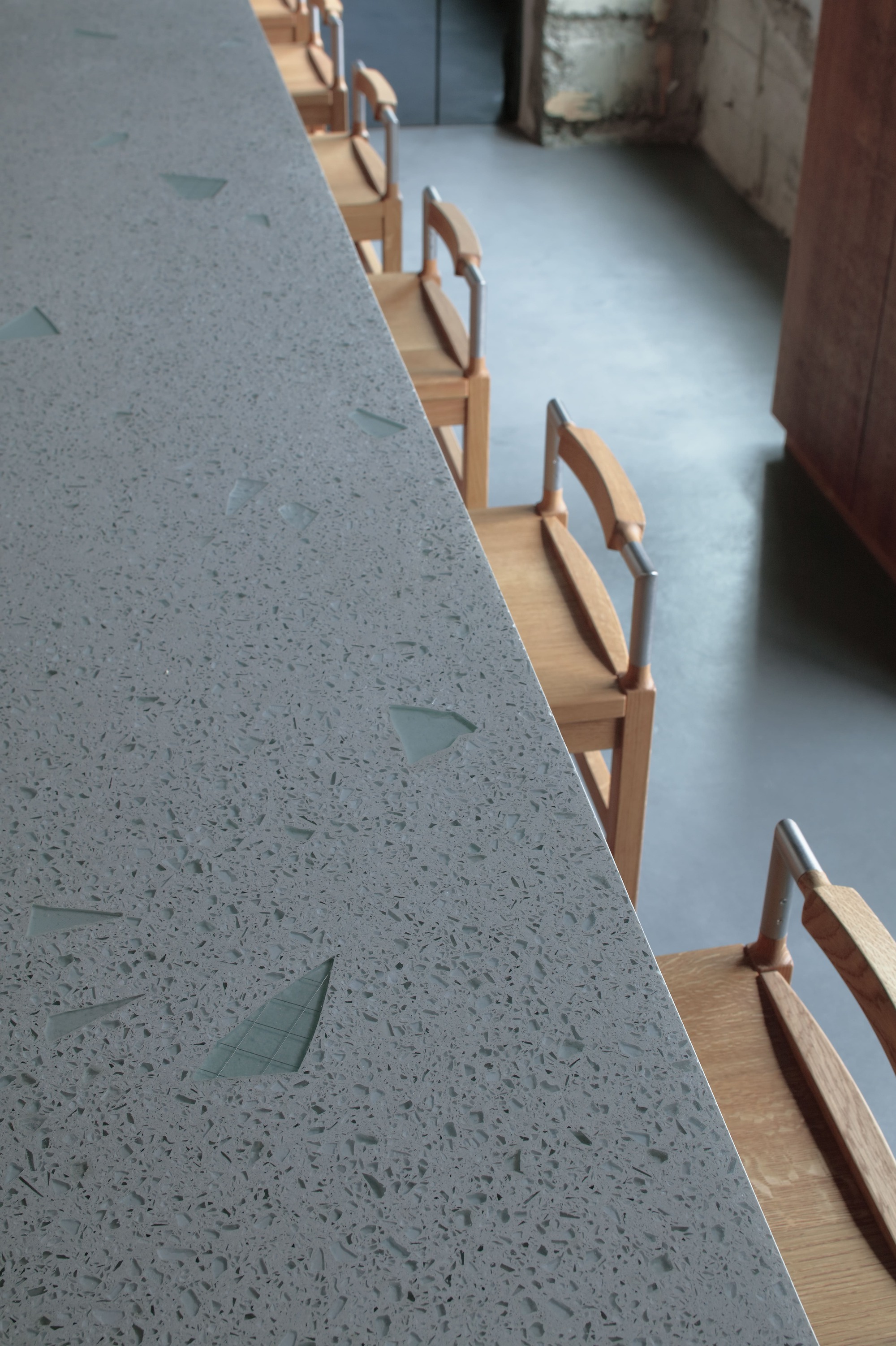 Close-up of terrazzo counter edge meeting timber base with chair backs in low light