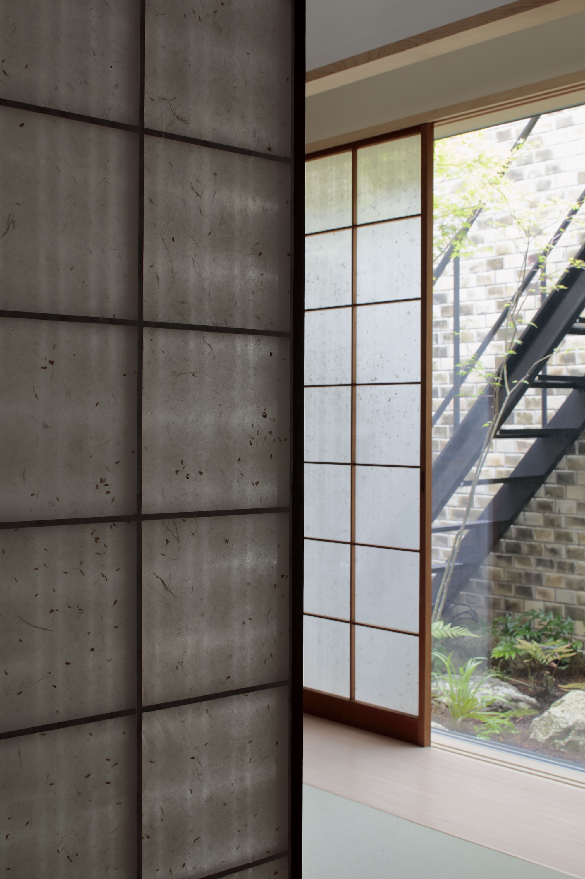 Shoji screen and board-formed concrete wall beside a courtyard garden with steel stair