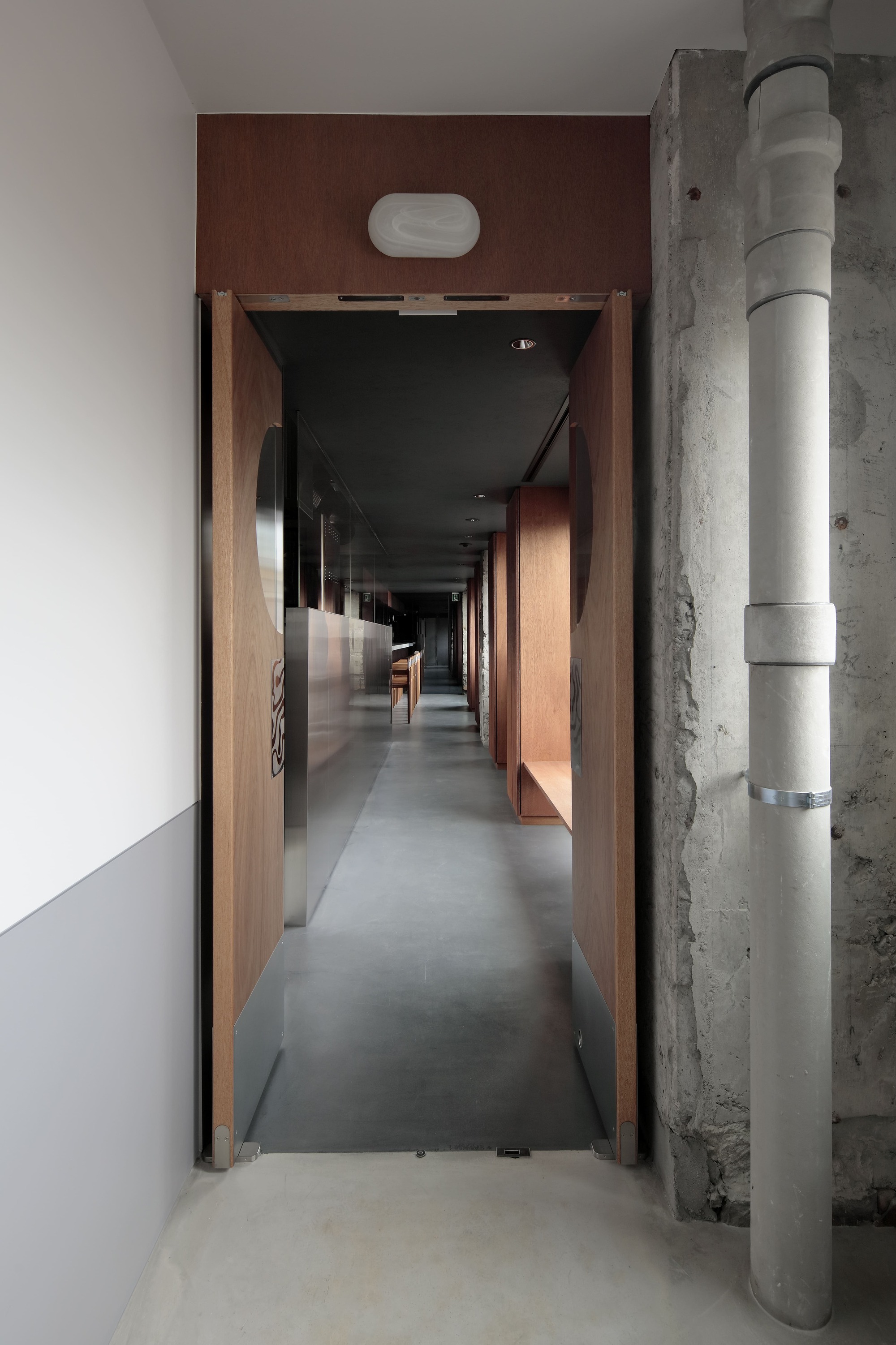 View through the walnut framed doorway into a corridor with polished concrete flooring and timber panelling