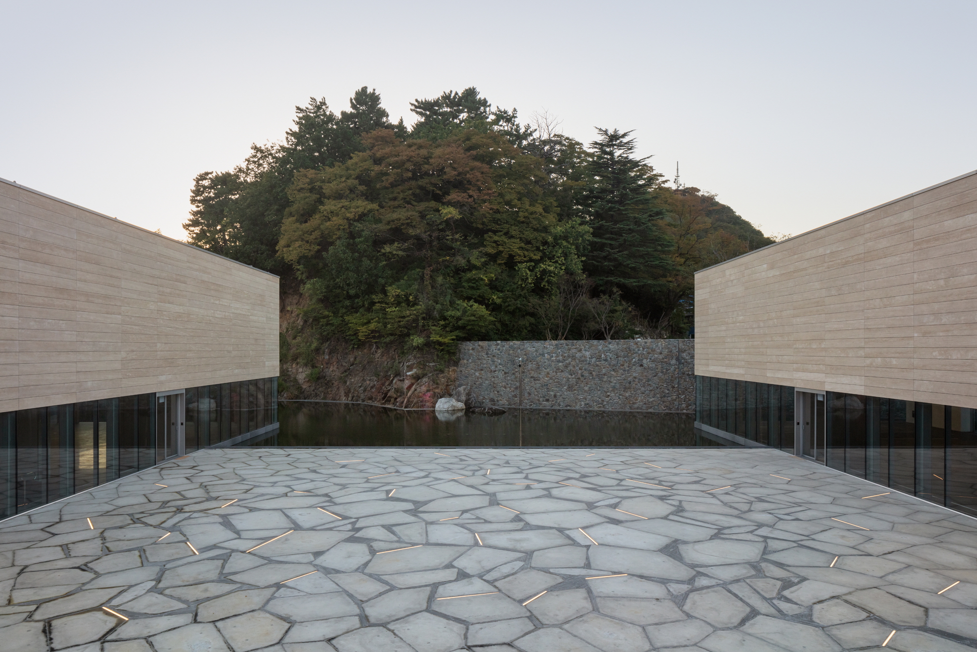 Polygonal stone paving in a courtyard opening toward a reflecting pool and forested hill