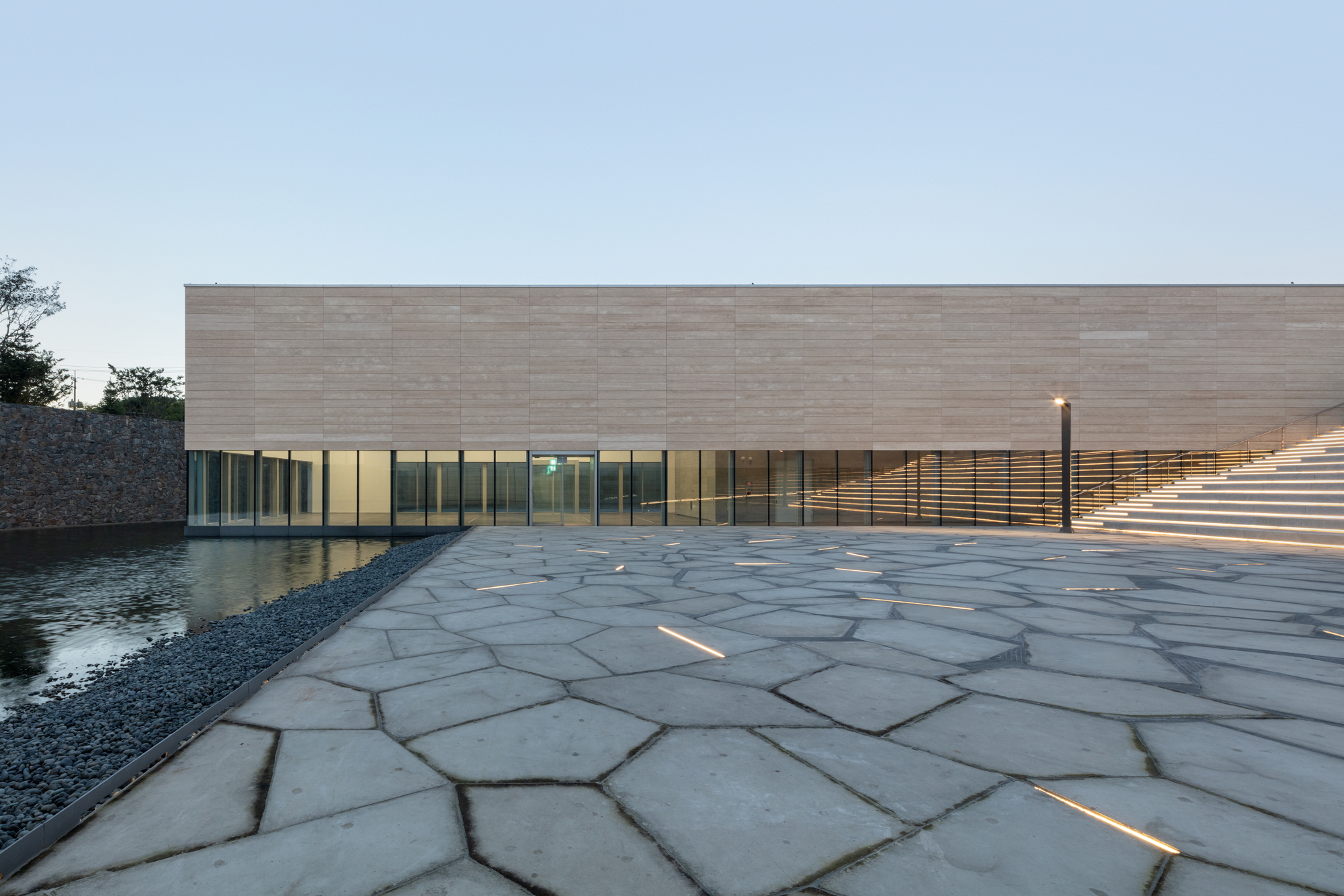 Low-angle view of the polygonal stone paving extending toward glass facade at twilight
