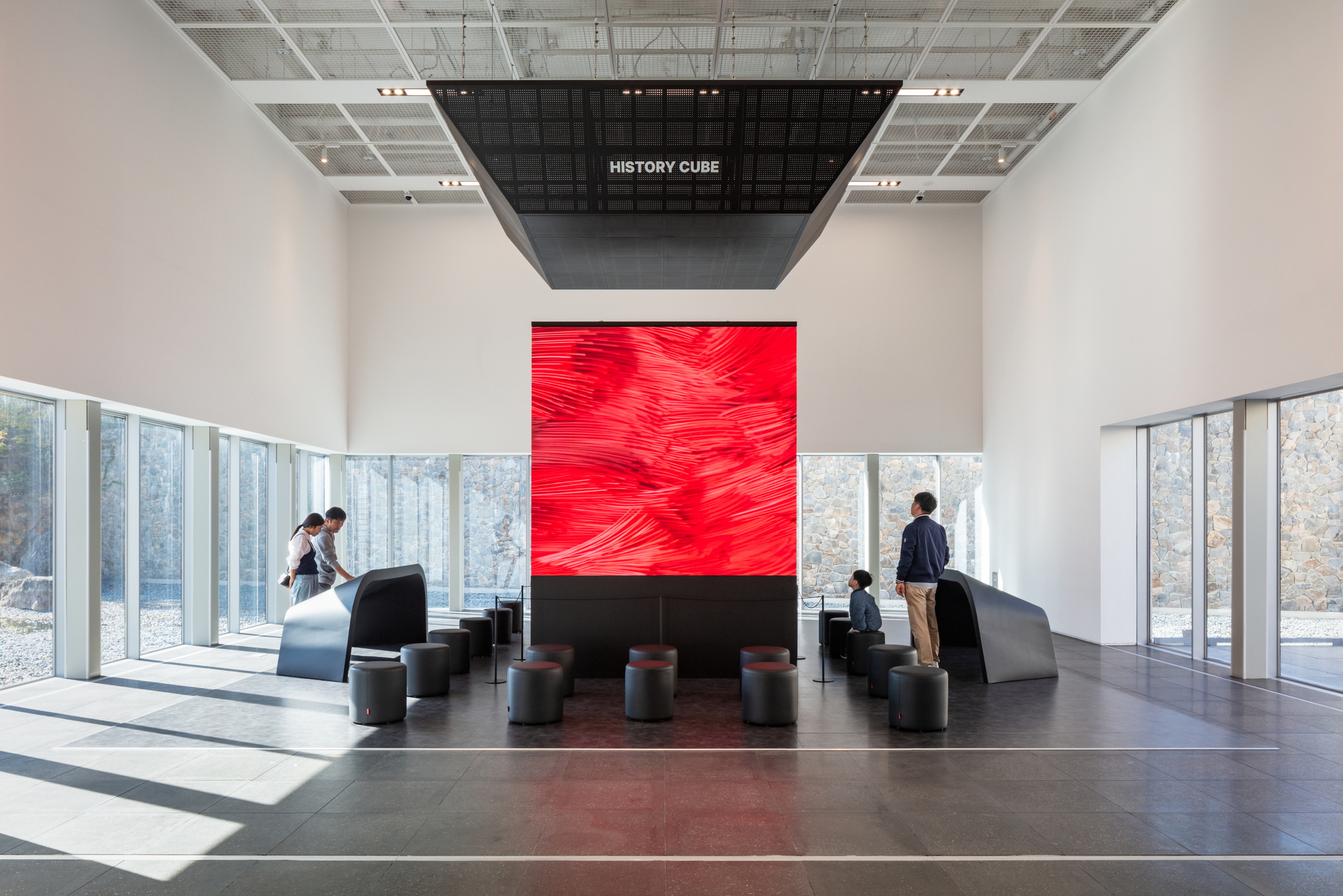 Central lobby with red digital display wall and ceiling-mounted cube beneath a gridded ceiling