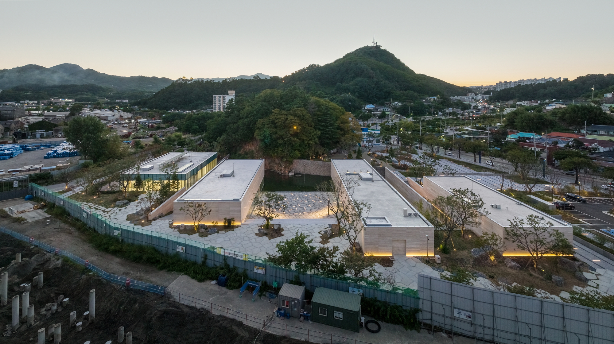 Aerial view of the low-lying pavilion complex with flat roofs and preserved trees at dusk
