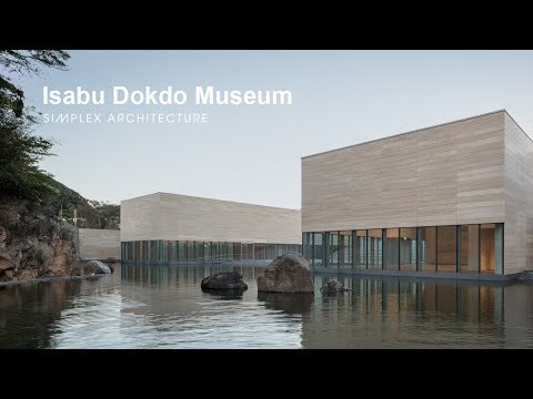 Horizontal timber-clad volumes reflected in a still pond with moss-covered rocks at dusk
