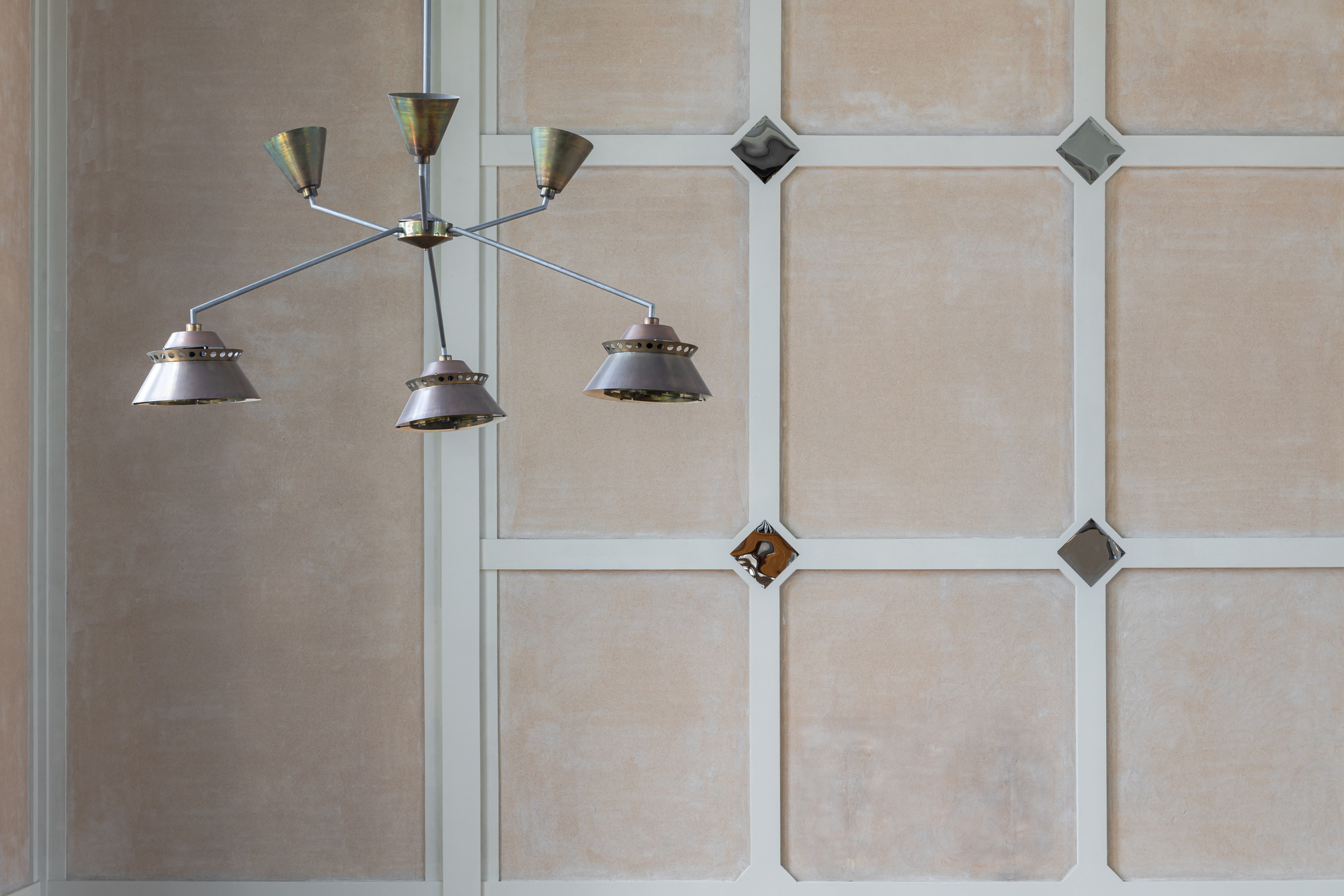 Multi-arm chandelier hanging against wall panel grid with diamond-shaped glass inserts and white trim
