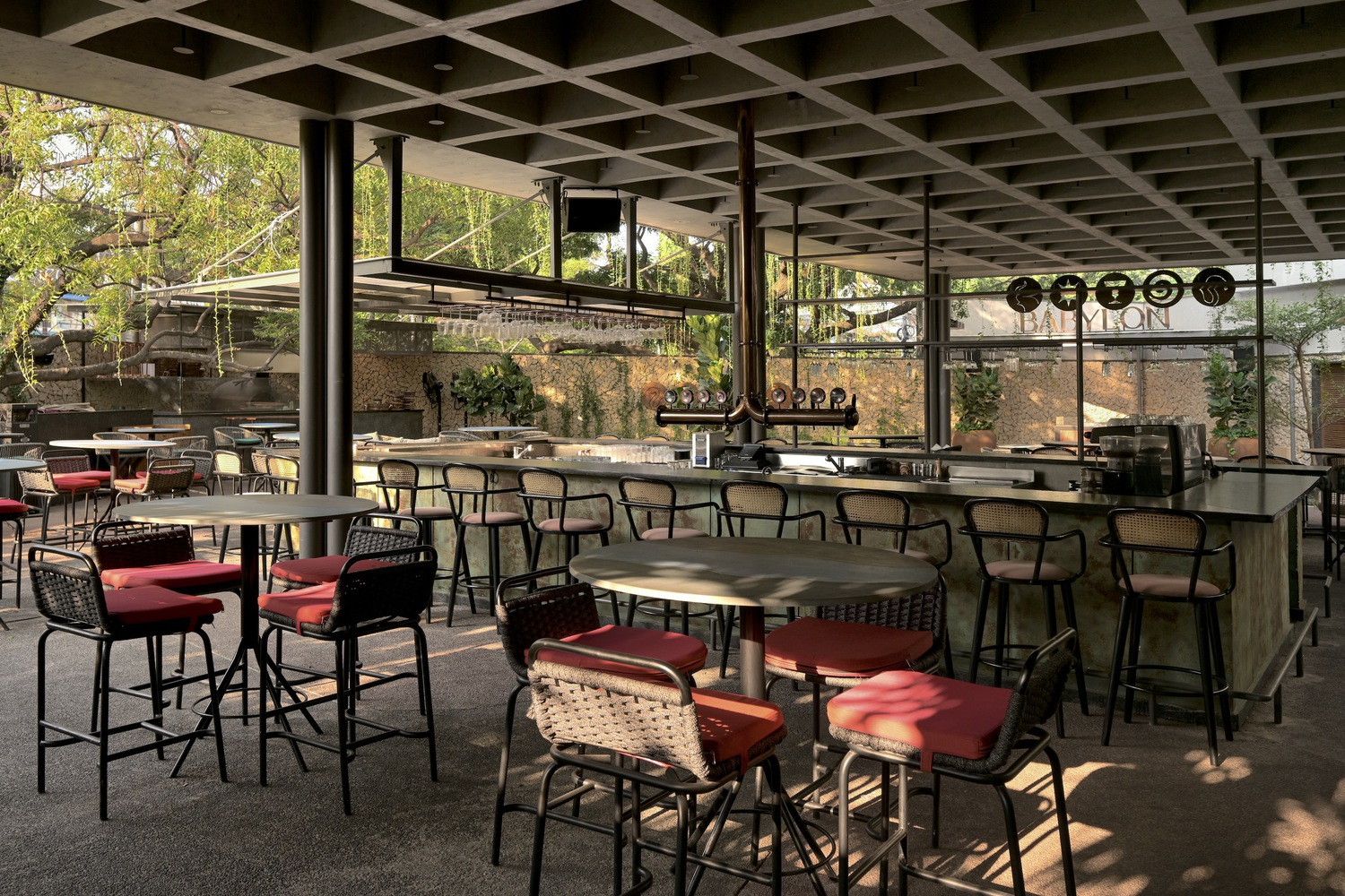 Bar seating area under coffered concrete ceiling with red cushioned stools and filtered afternoon light