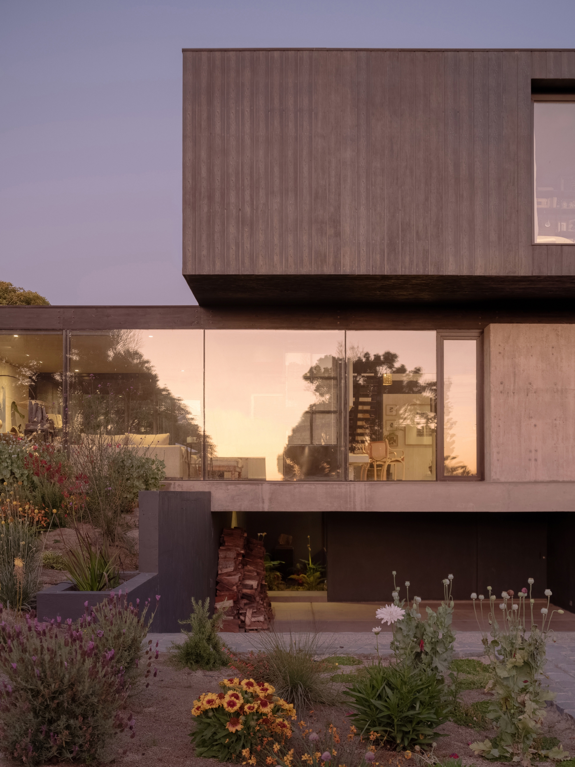 Stacked volumes with timber cladding and floor-to-ceiling glazing overlooking a planted terrace at twilight