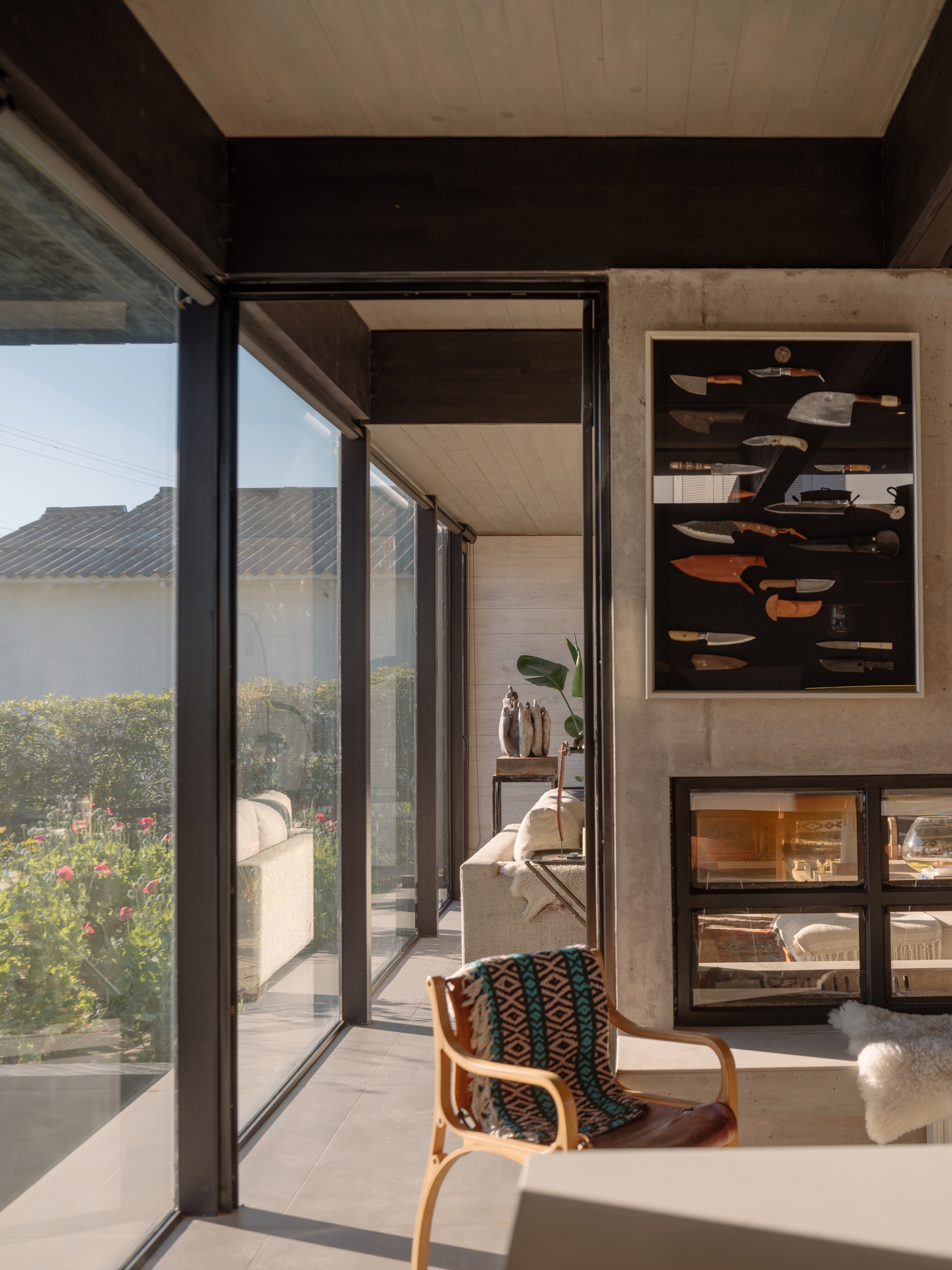 Interior corner with black steel framed glazing opening to a planted terrace in afternoon light