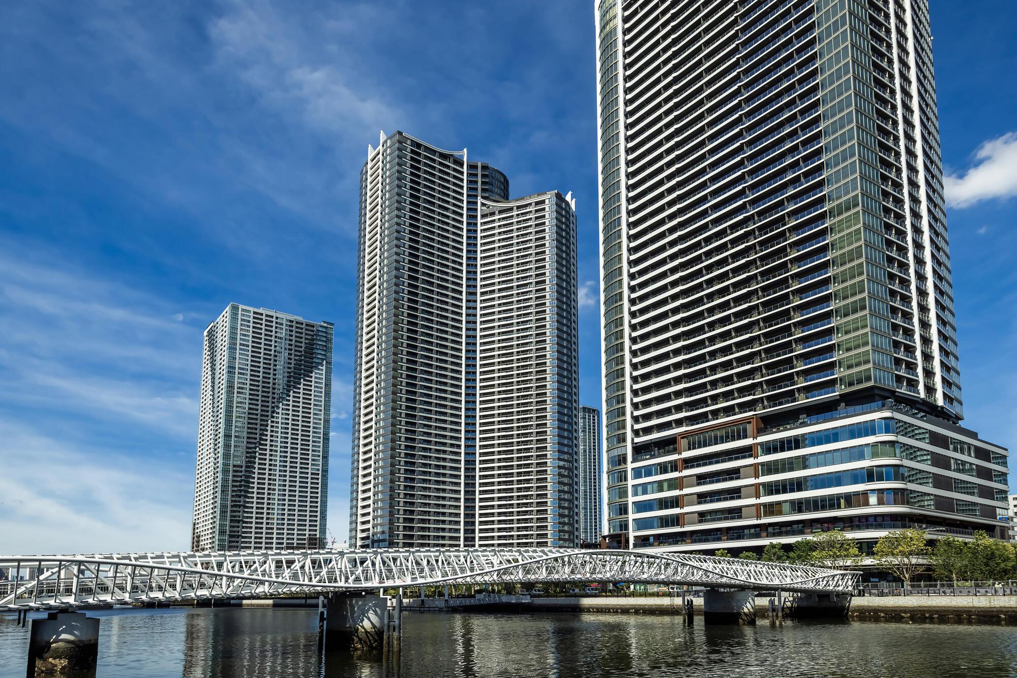Curved pedestrian bridge with triangulated steel structure crossing waterway beneath residential towers