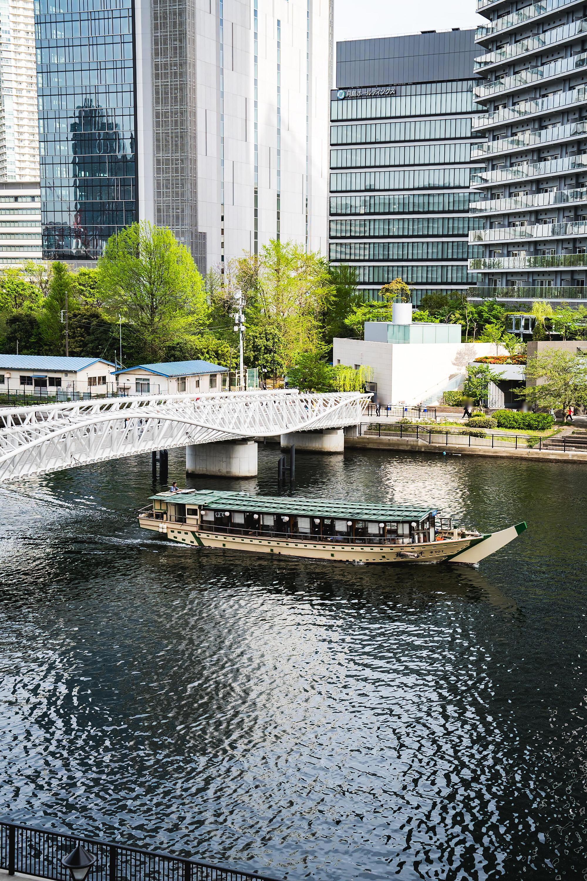 White lattice pedestrian bridge spanning a canal with a tourist boat passing beneath in spring
