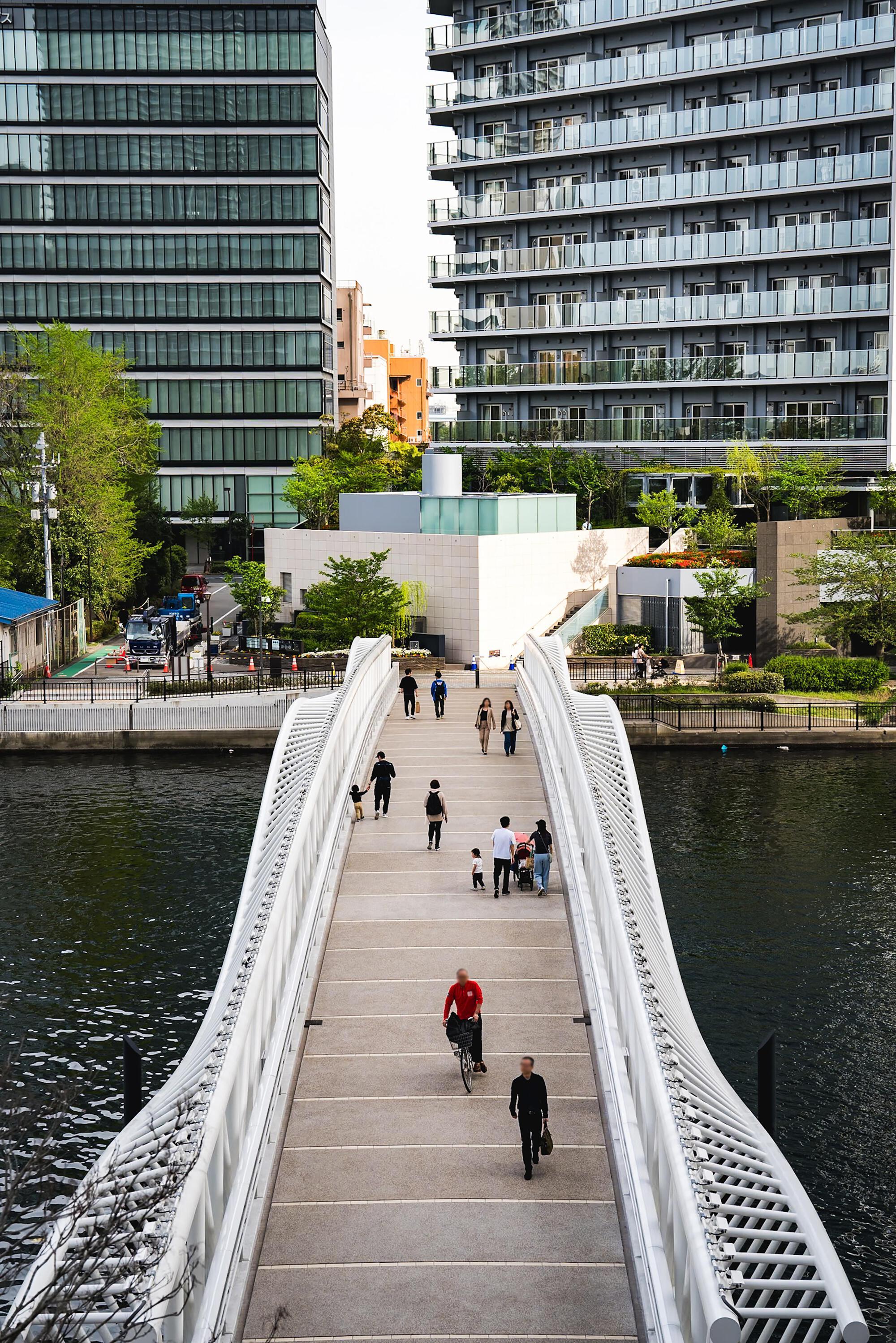 View along the timber deck of the bridge with pedestrians and cyclists moving between glass towers