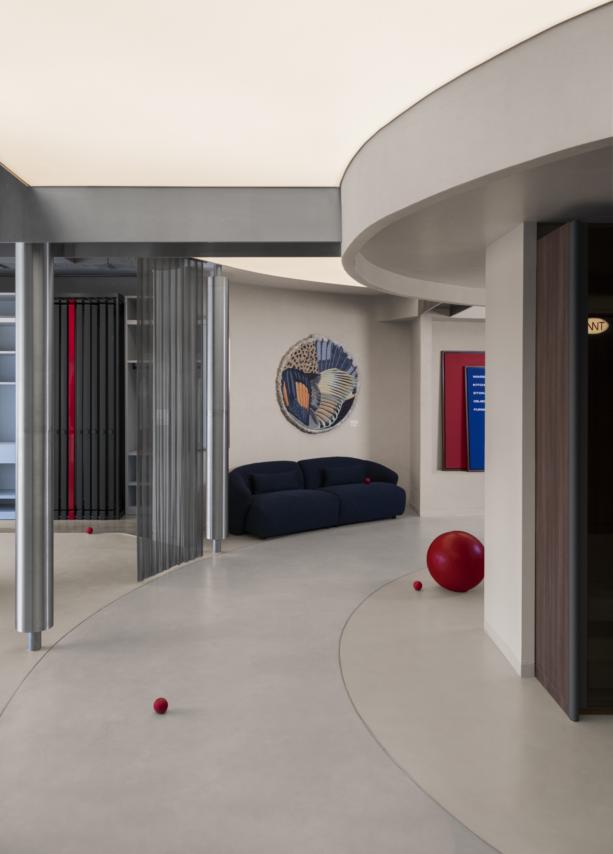 View across the polished floor showing circular wall art, a navy sofa and scattered red spheres