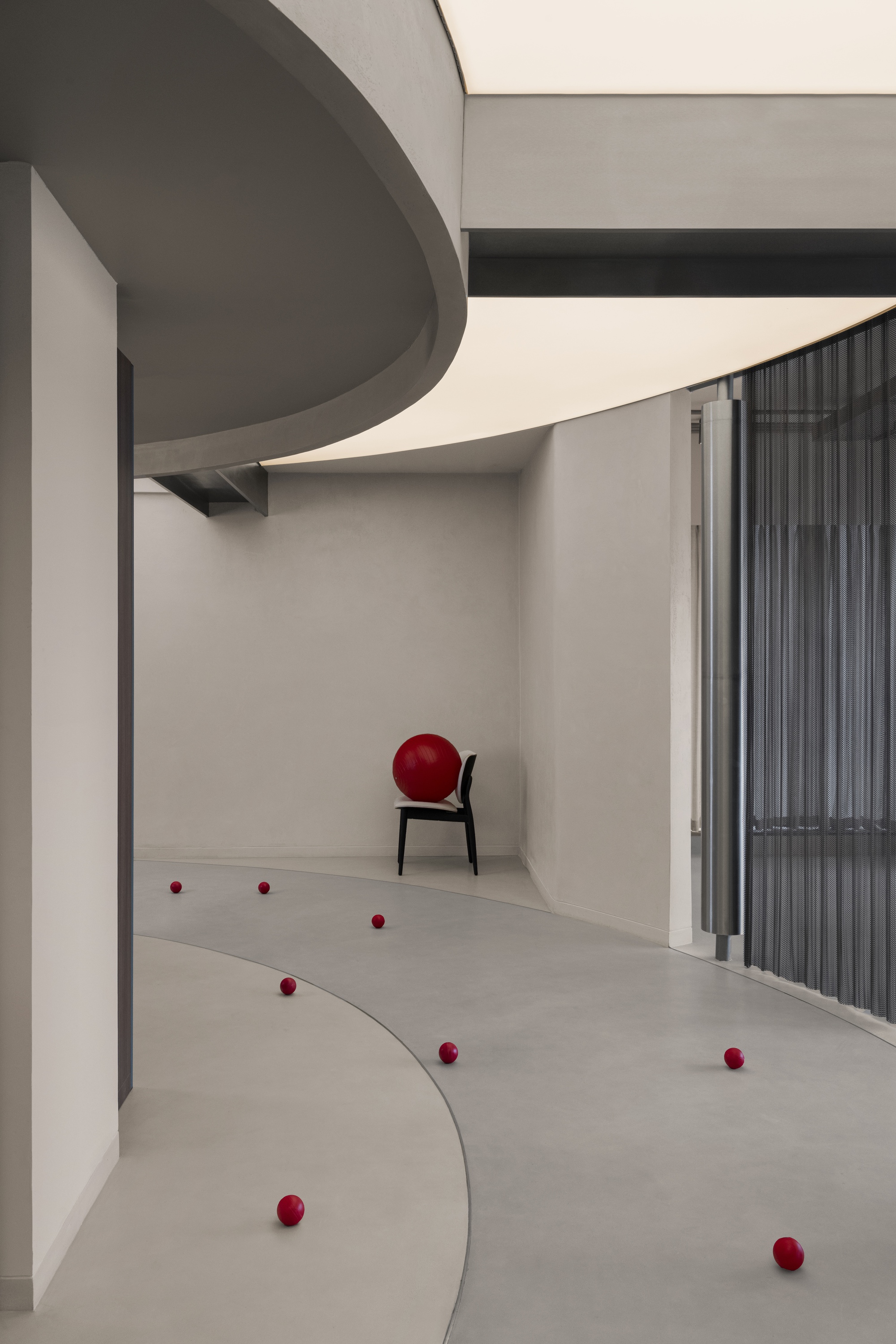 Gallery space with scattered red balls on curved floor sections and a black chair against the wall