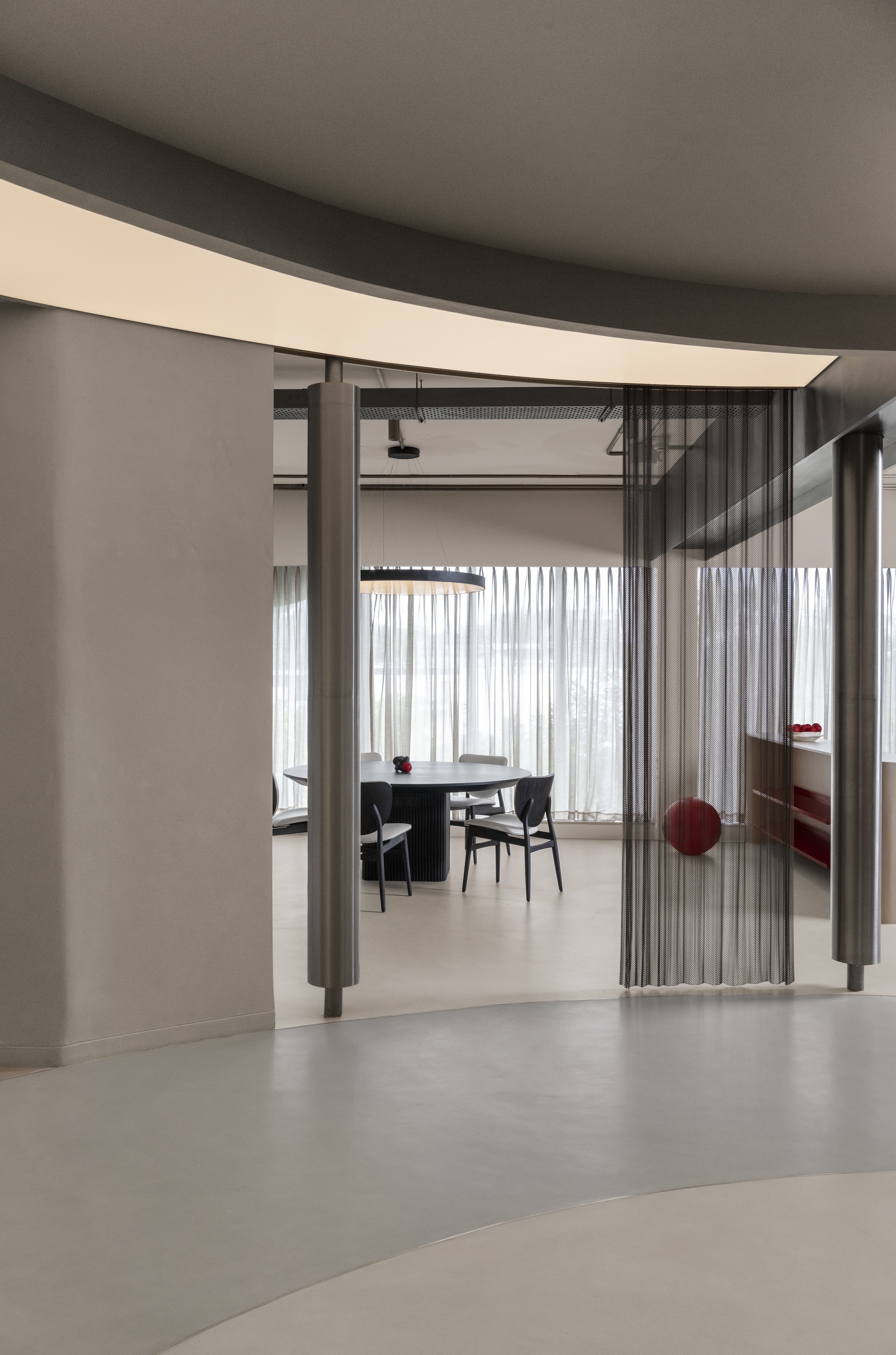 View through a folding metal screen partition into a dining area with sheer curtains and concrete floors