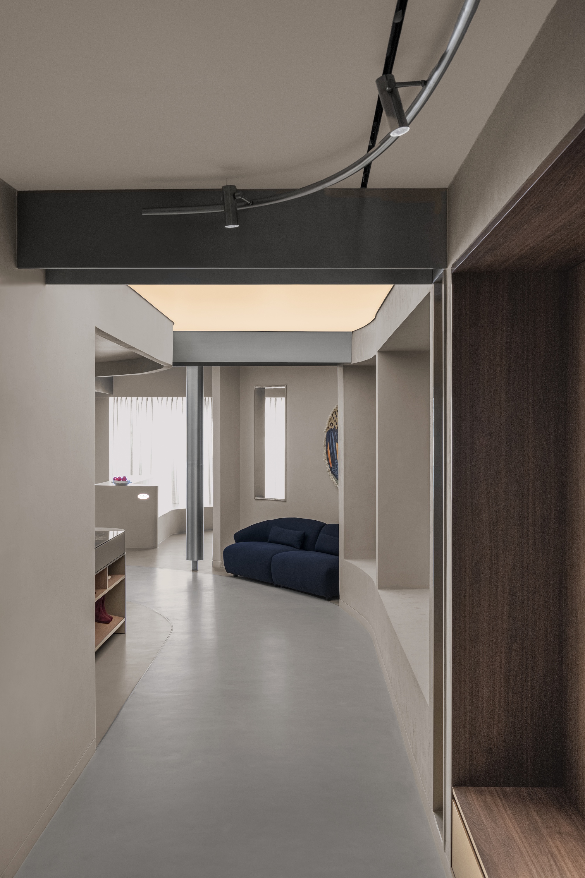 Corridor view showing recessed lighting cove above and a blue sofa in the adjacent room