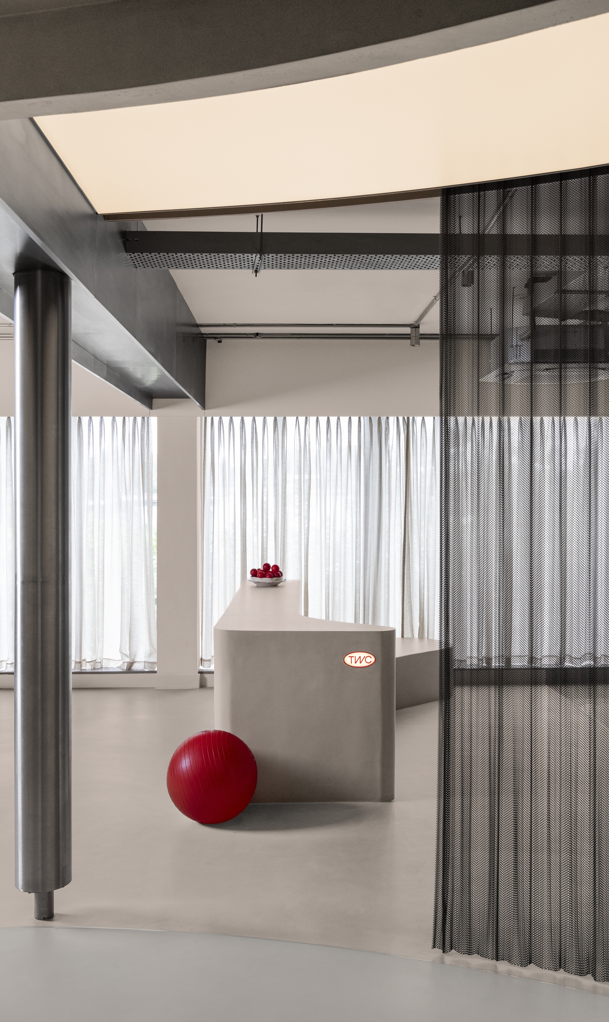 Interior view through metal mesh partition with red exercise ball on the polished floor and sheer curtains beyond