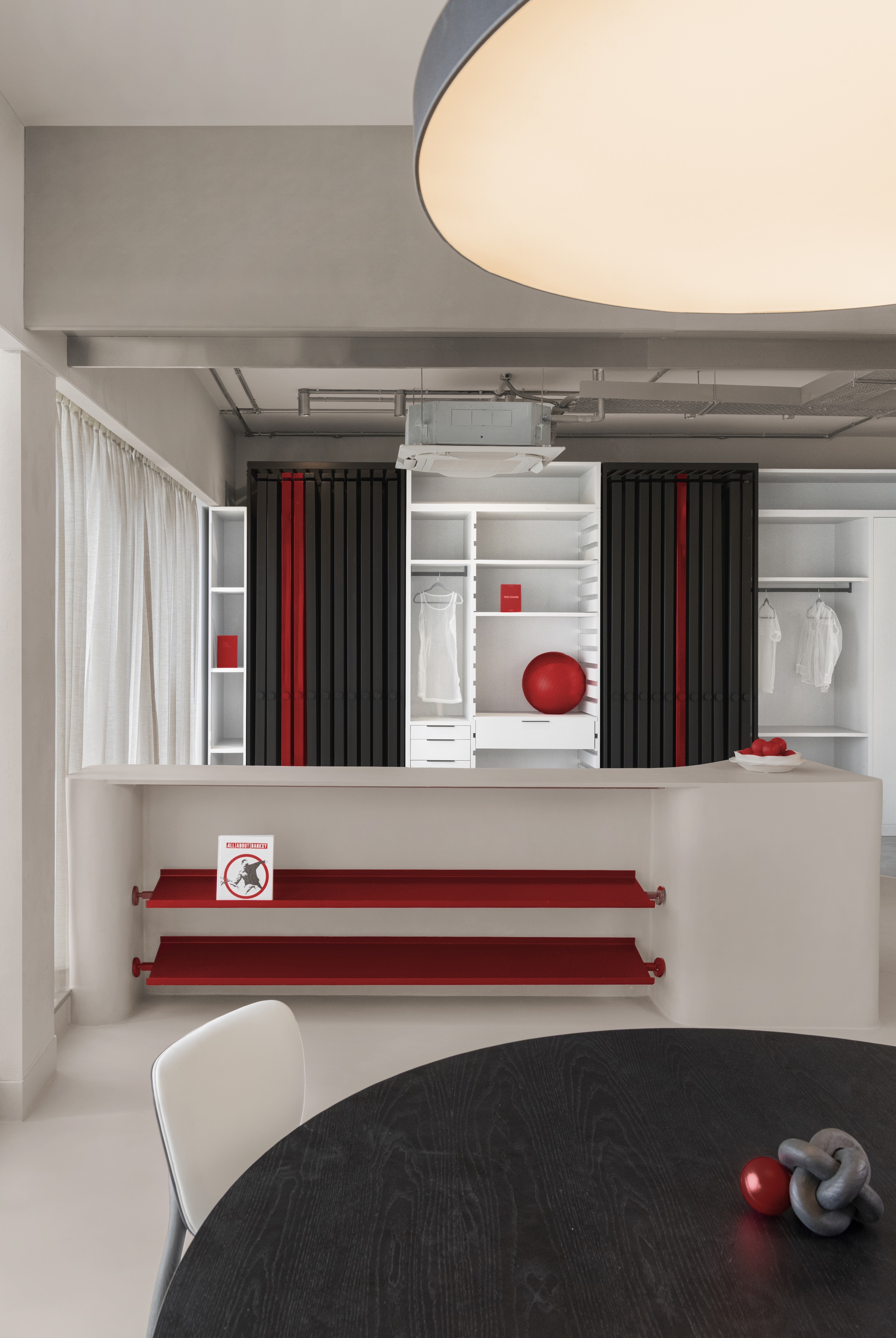 Wardrobe wall with pleated black curtains, white shelving, and red accent shelves beneath exposed ceiling ducts