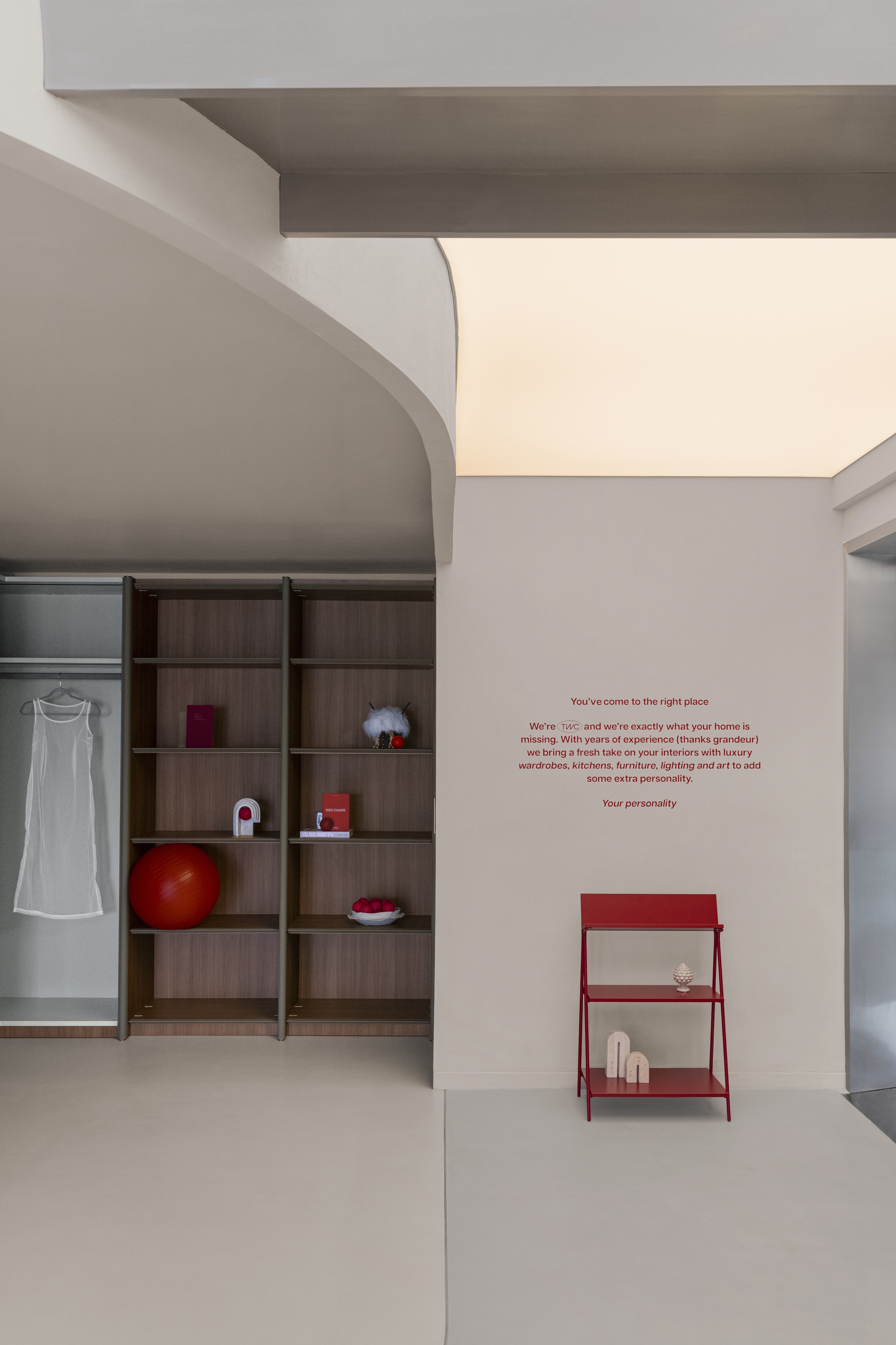 White wall with red text, a curved volume, timber shelving, and a red metal side table