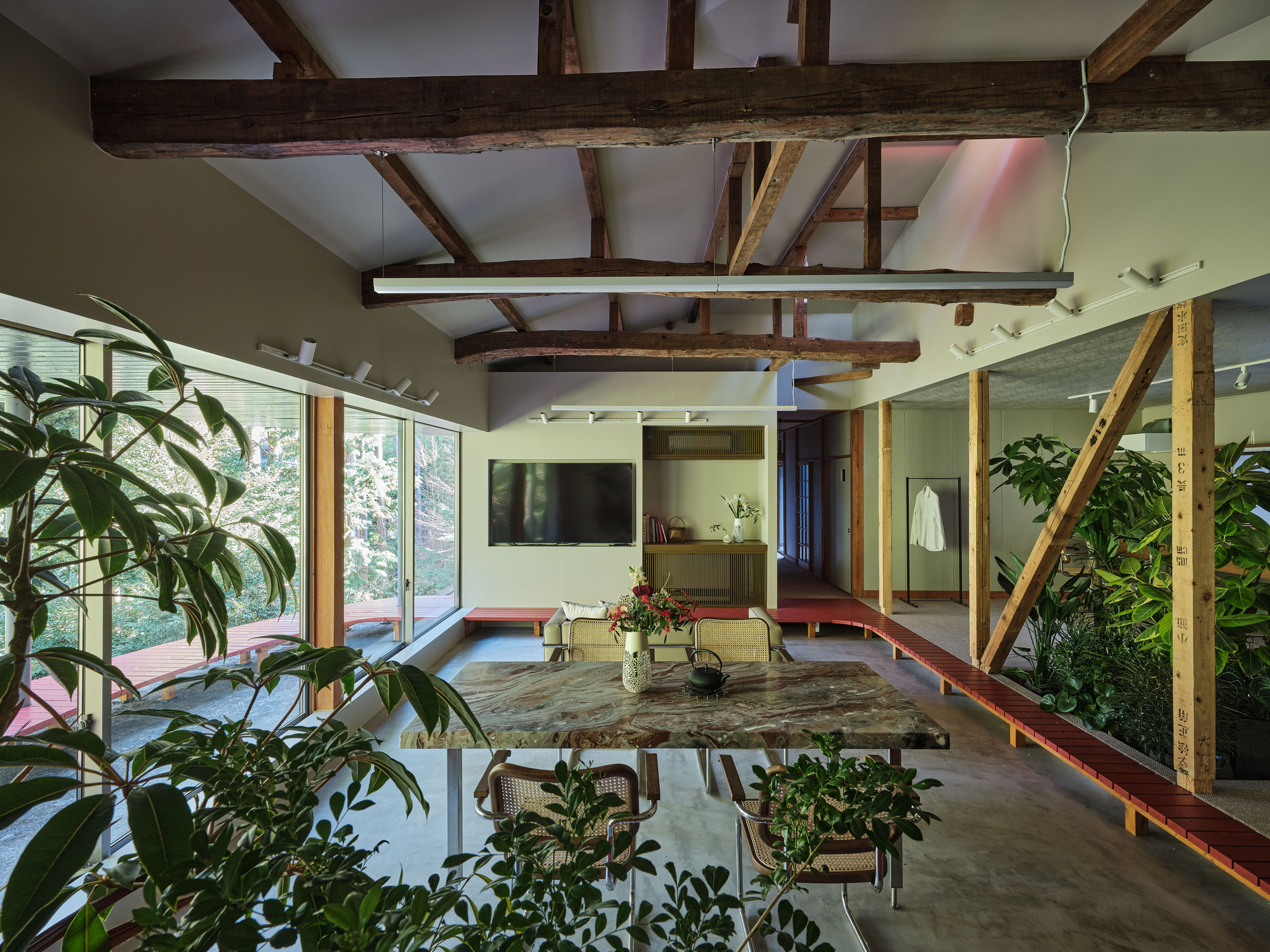 Open interior with exposed timber beams, planted beds and a reclaimed wood table beneath a mezzanine level