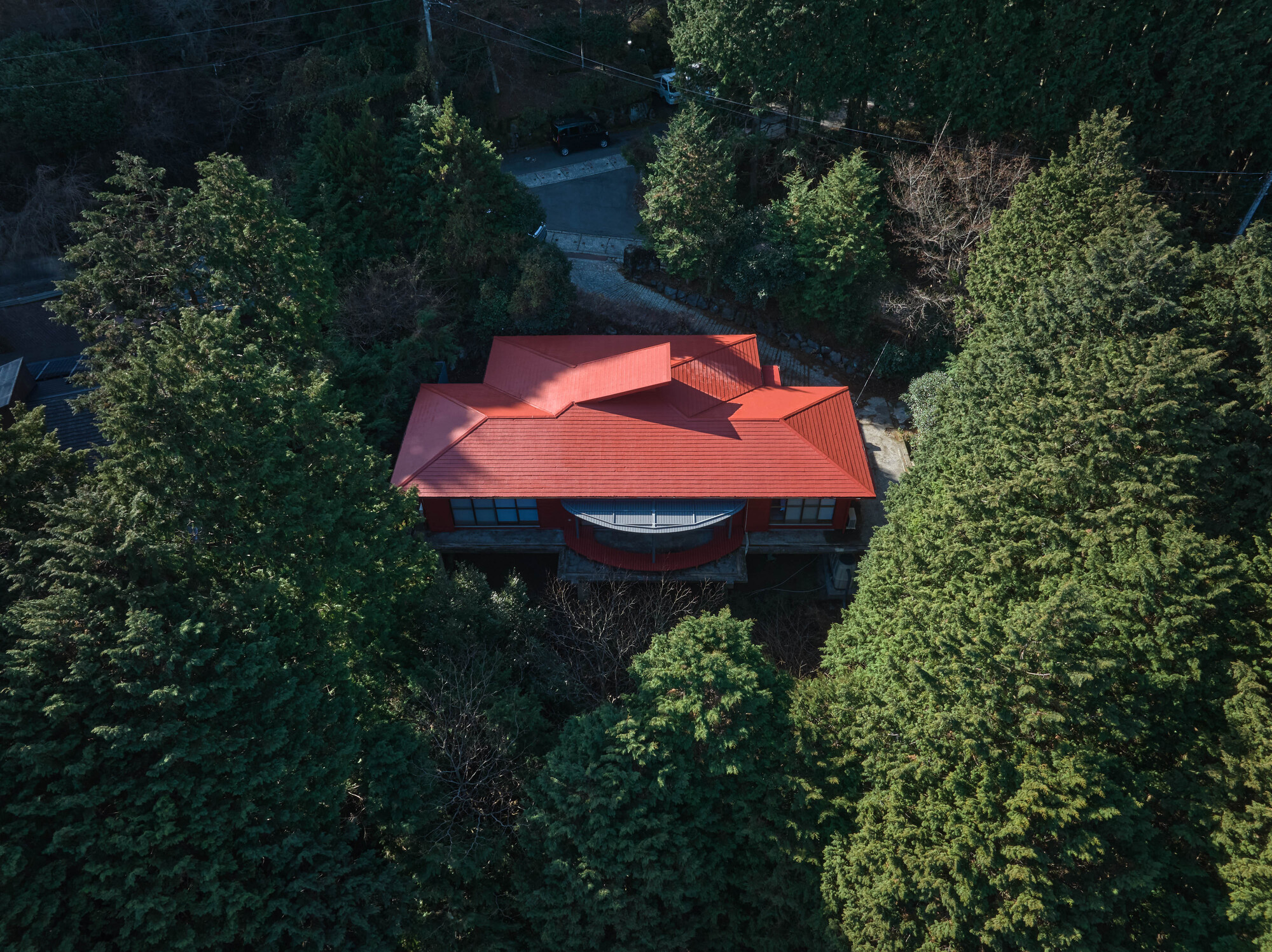 Aerial view of the red tiled roof with a curved center element nestled among dense forest canopy