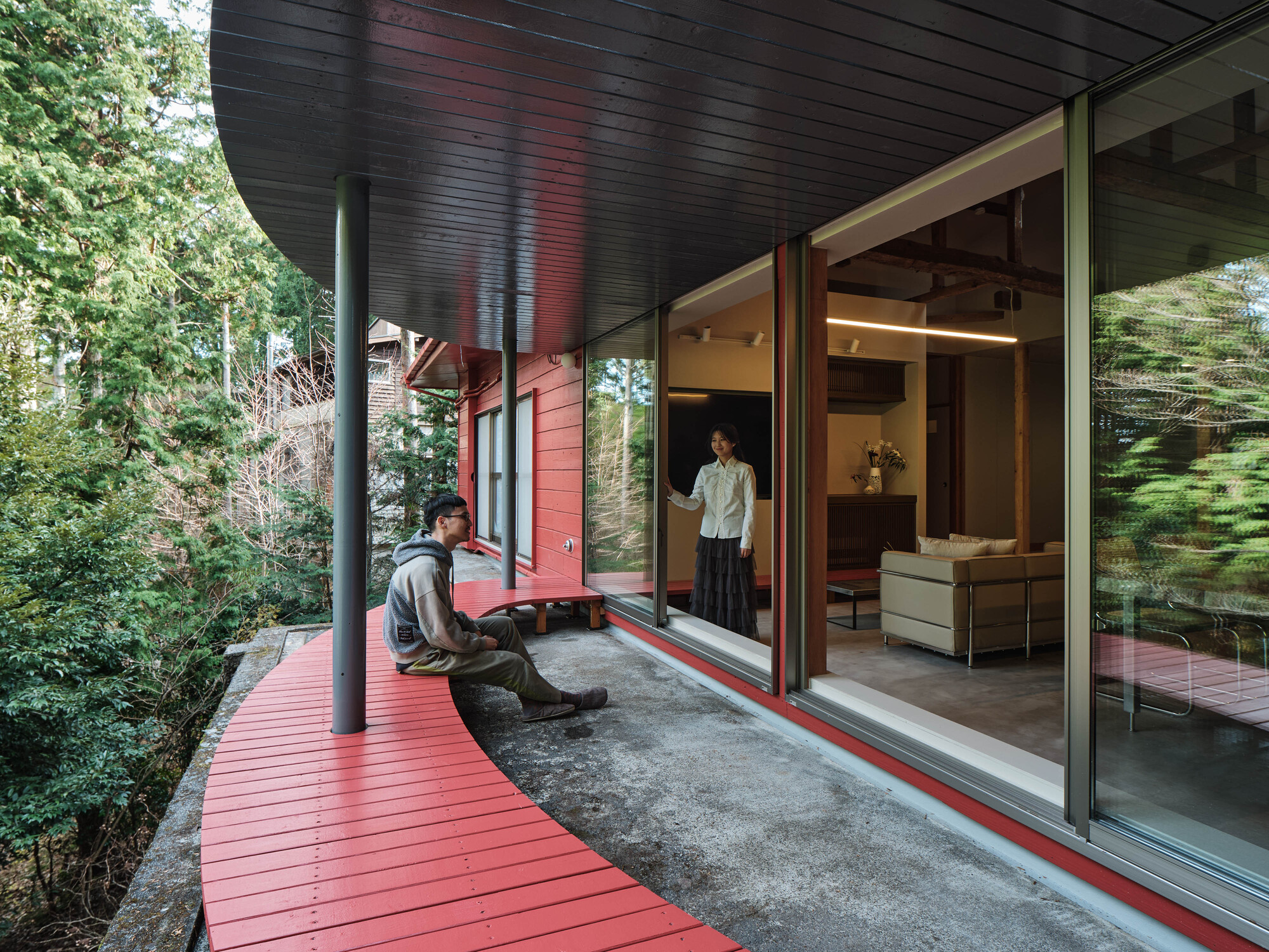 Covered deck with red planks and black soffit where two figures gather near sliding glass doors