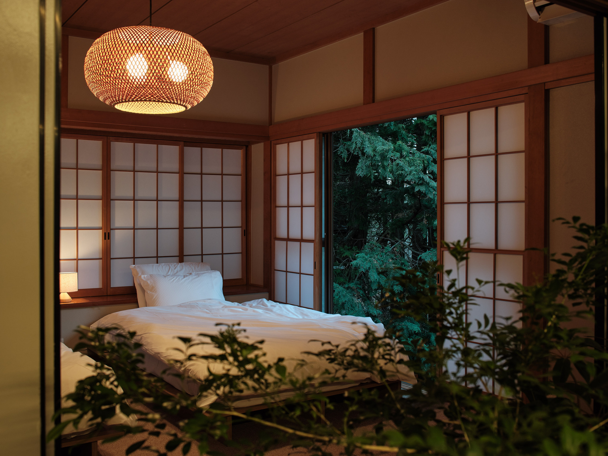Bedroom with translucent shoji screens and woven pendant light opening to evening forest beyond
