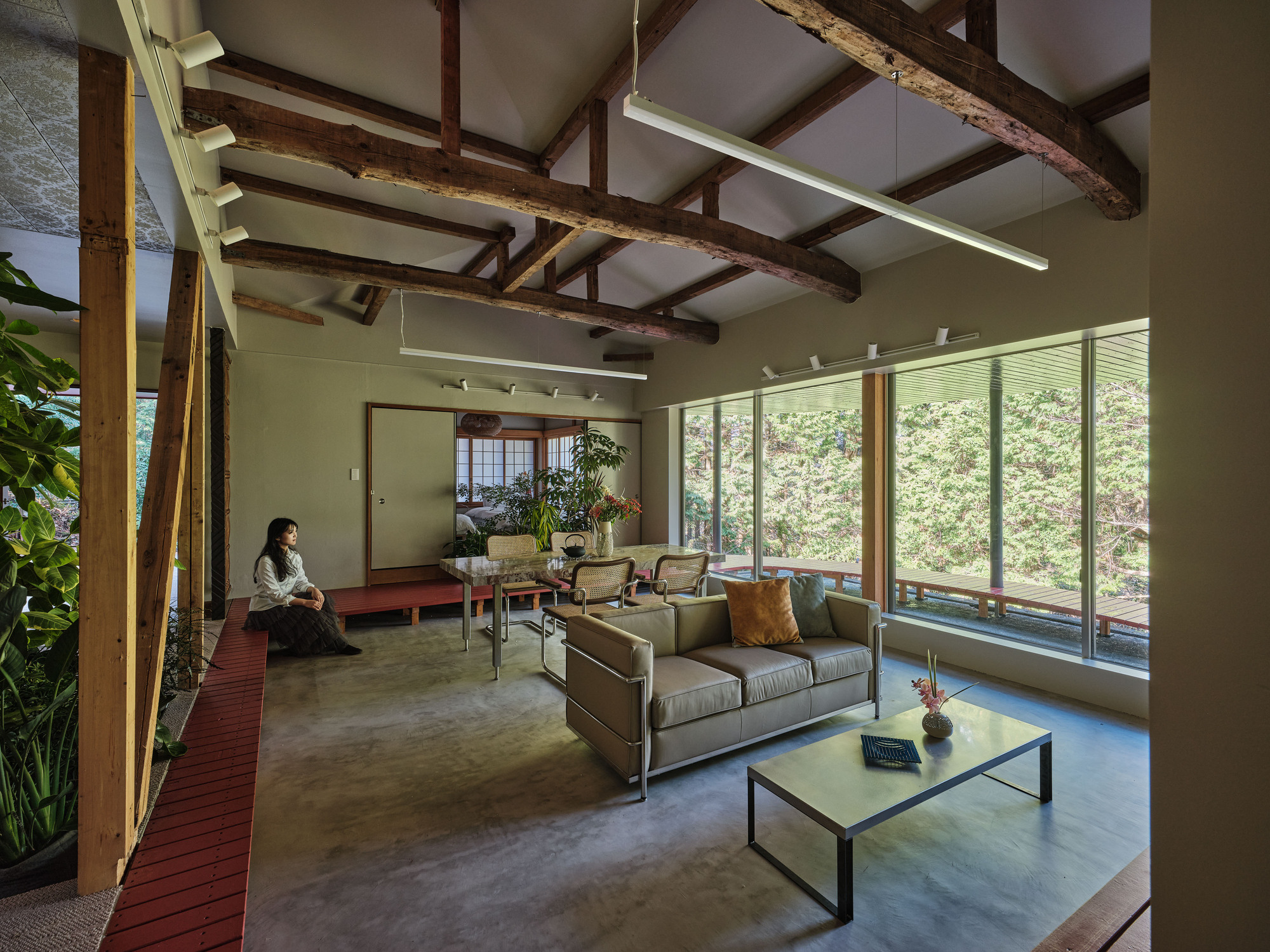 Living room with polished concrete floor and exposed timber ceiling beams with person seated on red platform