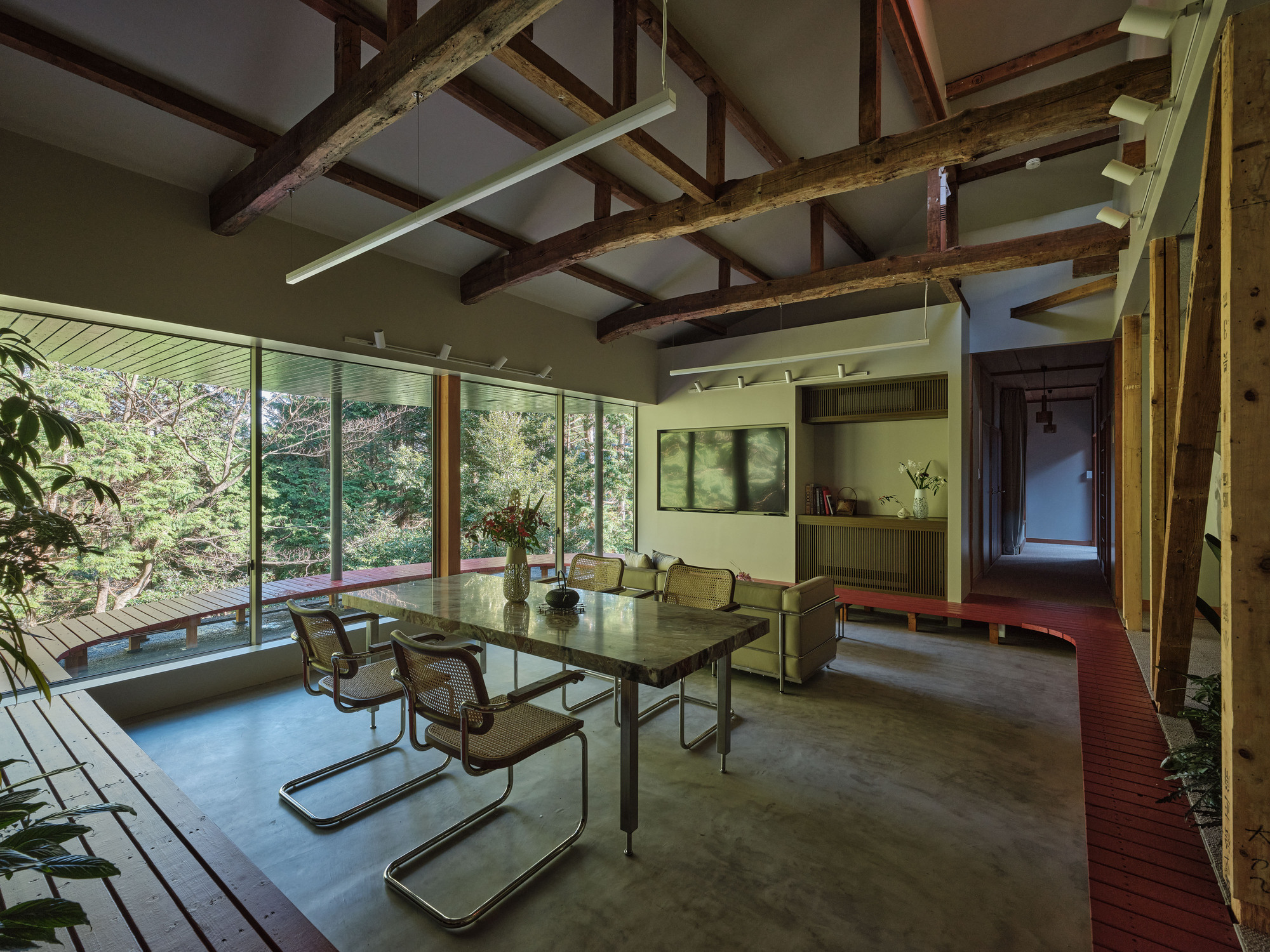 Dining area with glass table and cantilever chairs beneath exposed timber beam structure and linear lighting