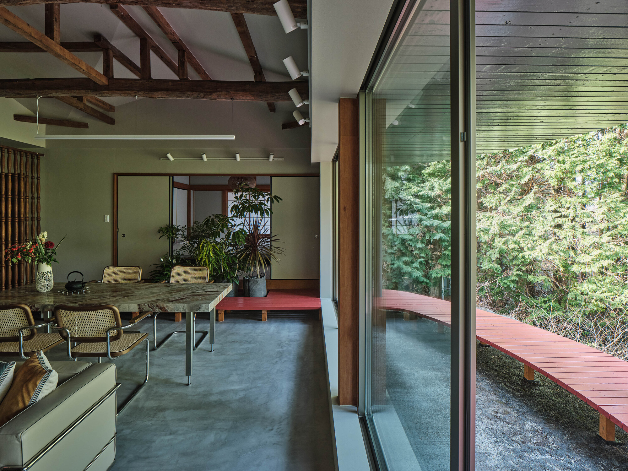 Interior view of dining area opening onto exterior red timber deck through sliding glass doors