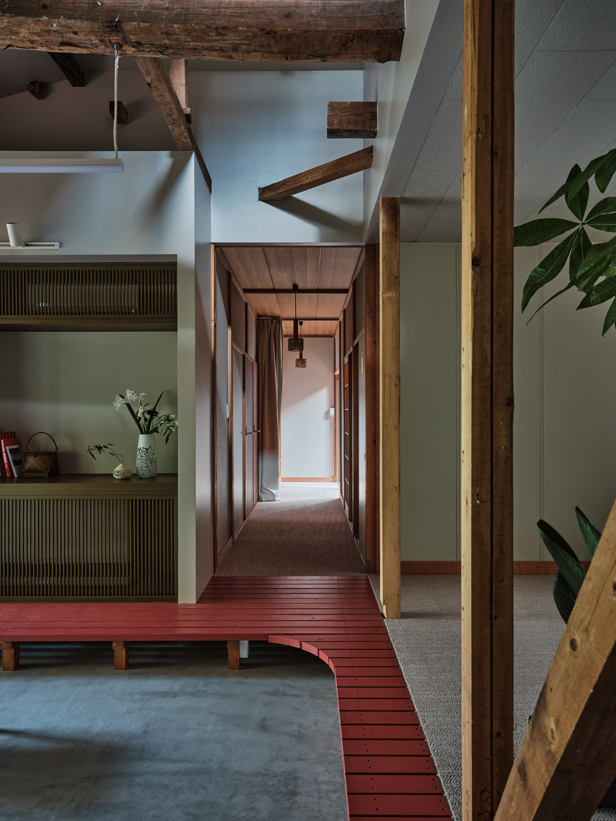 Raised red timber platform connecting interior spaces with exposed ceiling beams and olive green walls