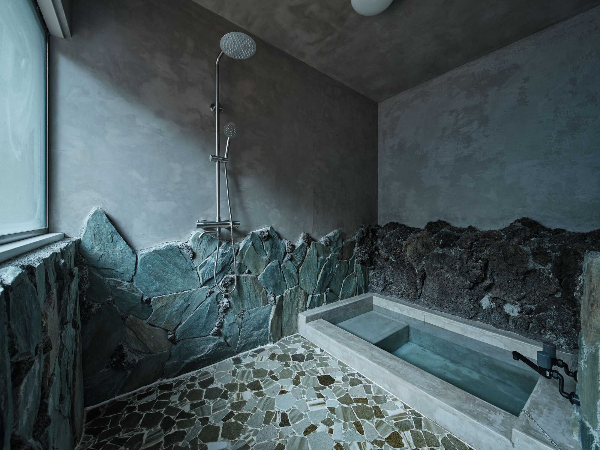 Bathroom with slate-clad mountain motif surround and concrete soaking tub with mosaic pebble floor