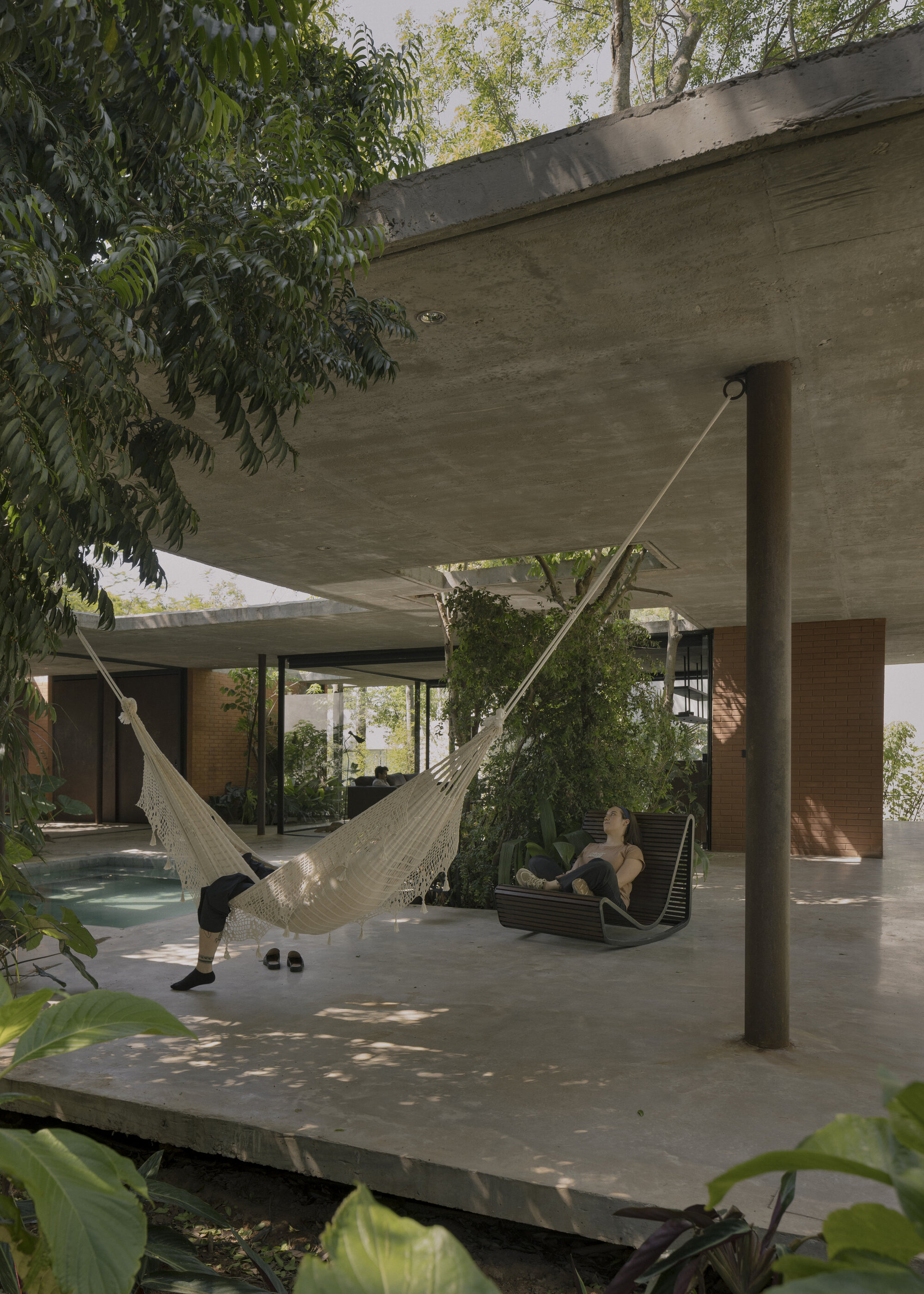 Cantilevered concrete terrace with hammocks and a person beneath dappled tree shade