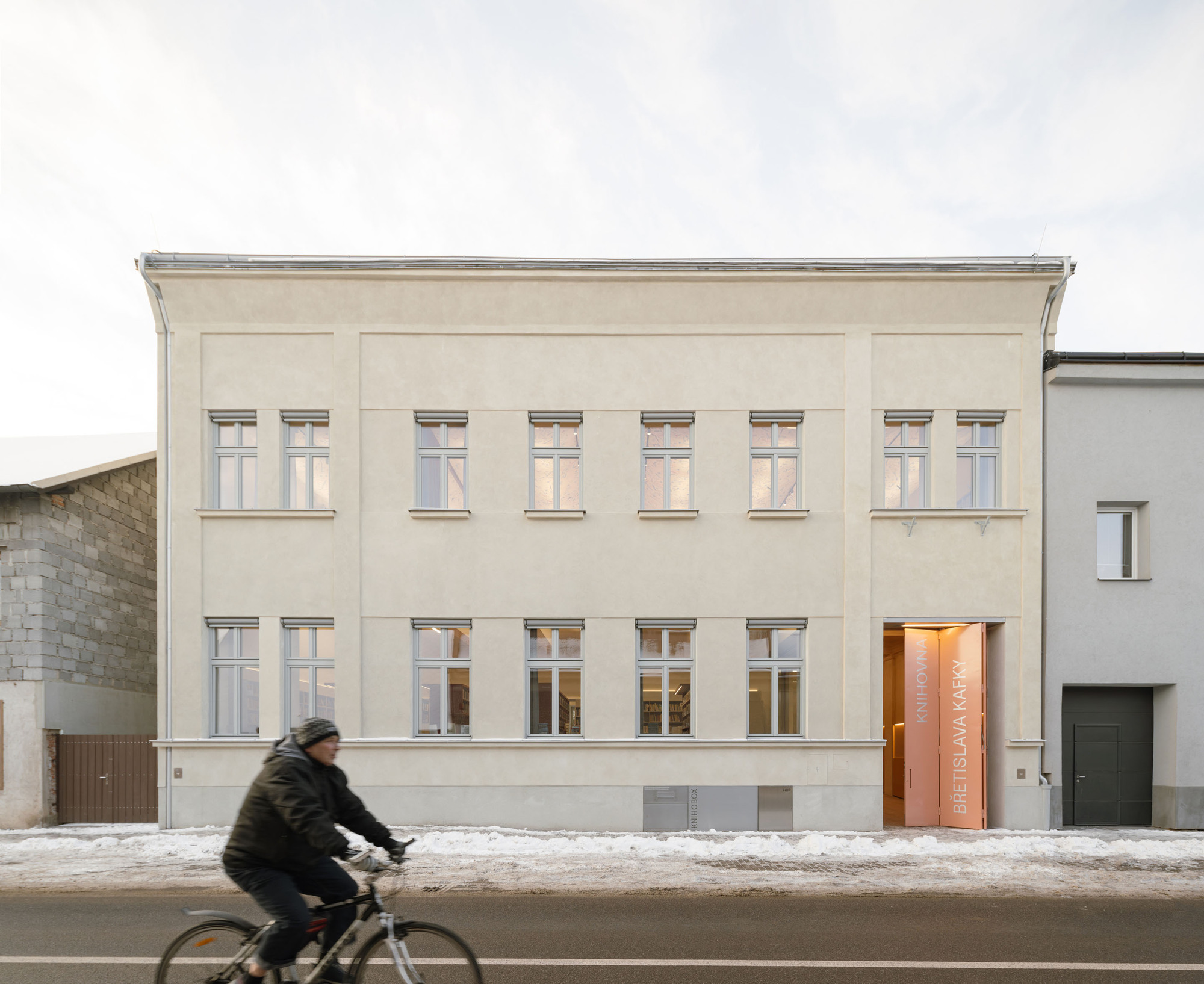 Street facade with pale plaster walls and symmetrical windows as a cyclist passes in winter