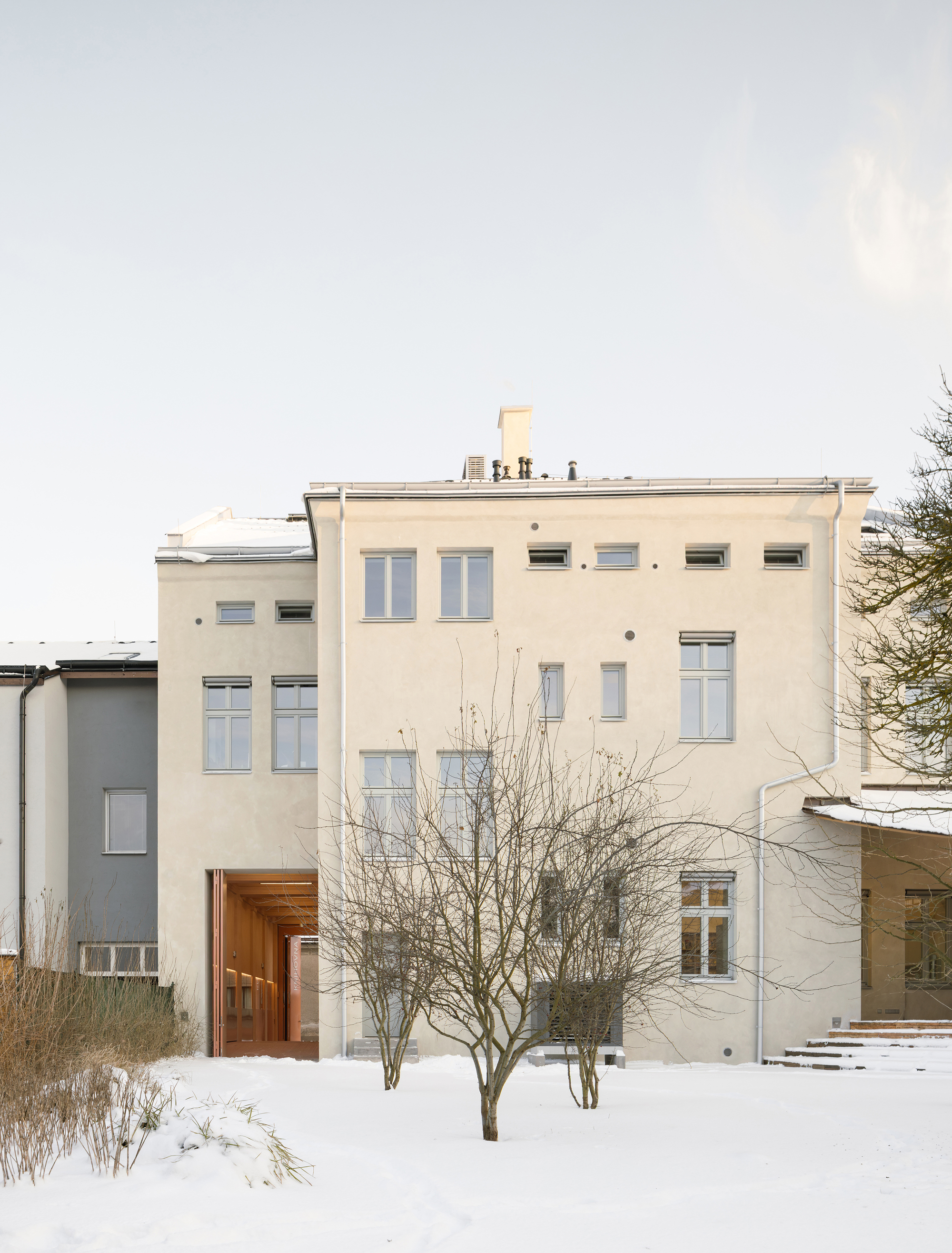 Rear elevation with pale stucco, varied window sizes, and bare winter trees in snow