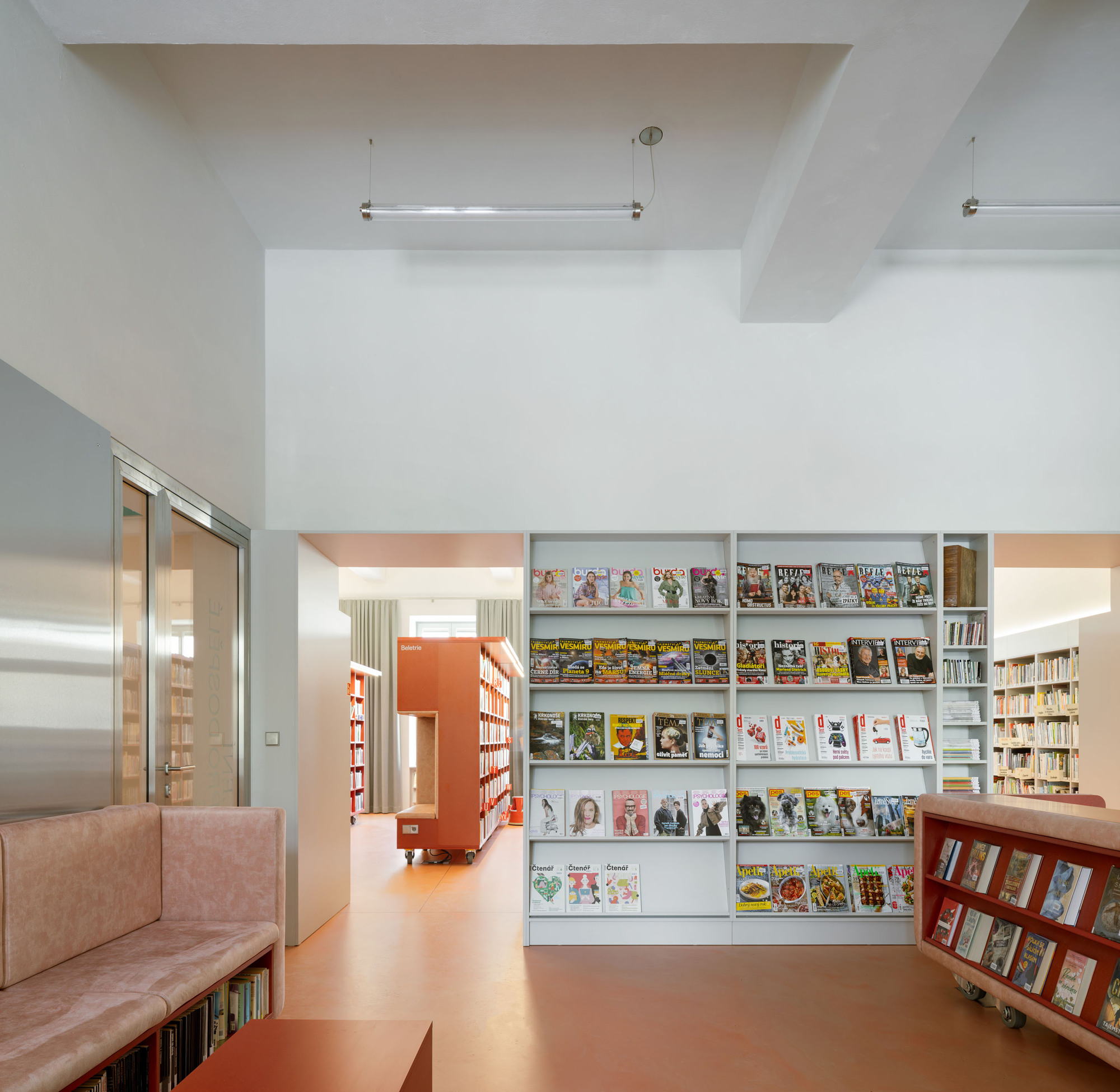 Library reading area with white magazine display shelves and coral rubber flooring under natural light