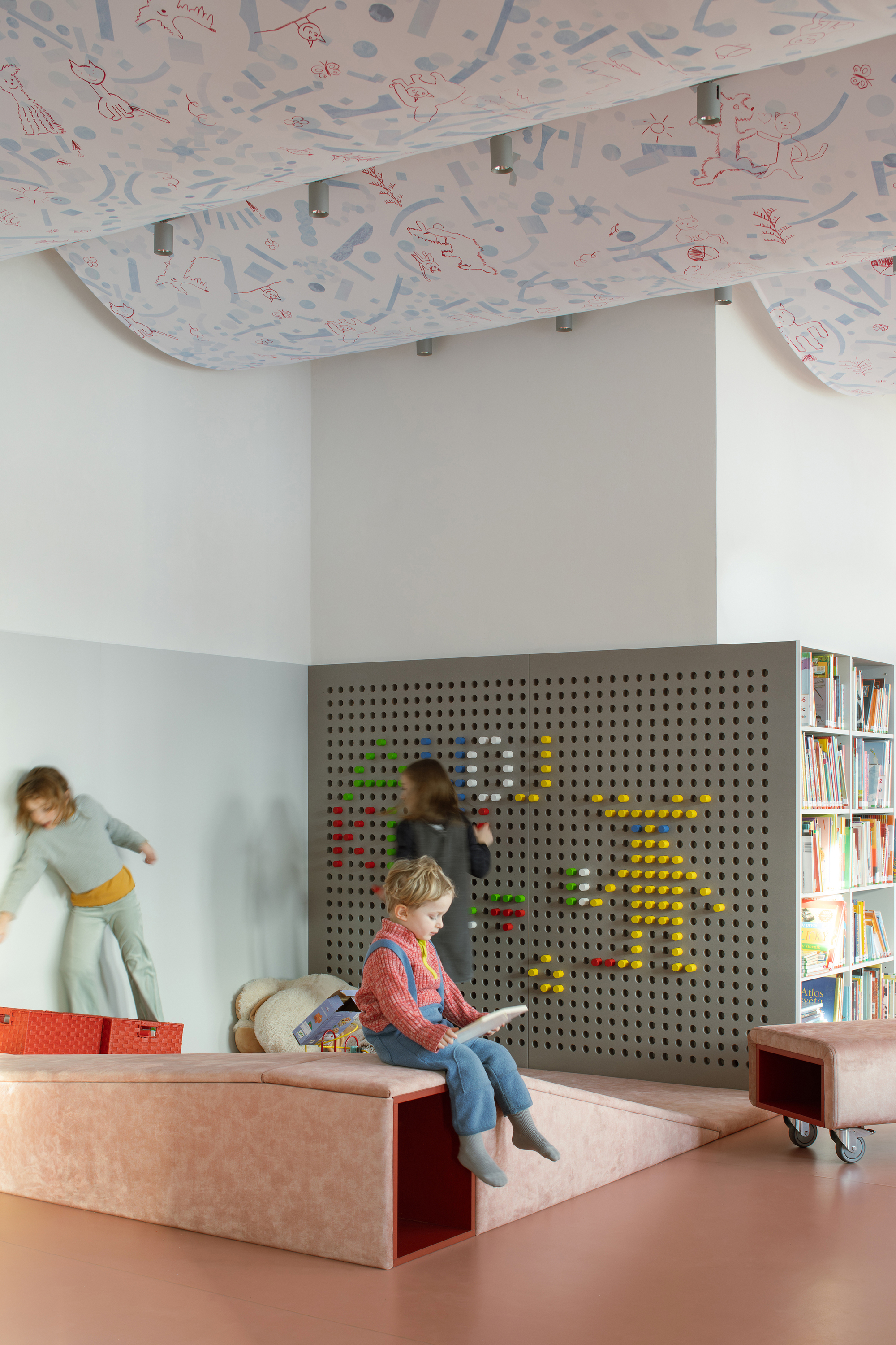 Pegboard wall with colored toys and children playing on stepped platform under draped illustrated ceiling