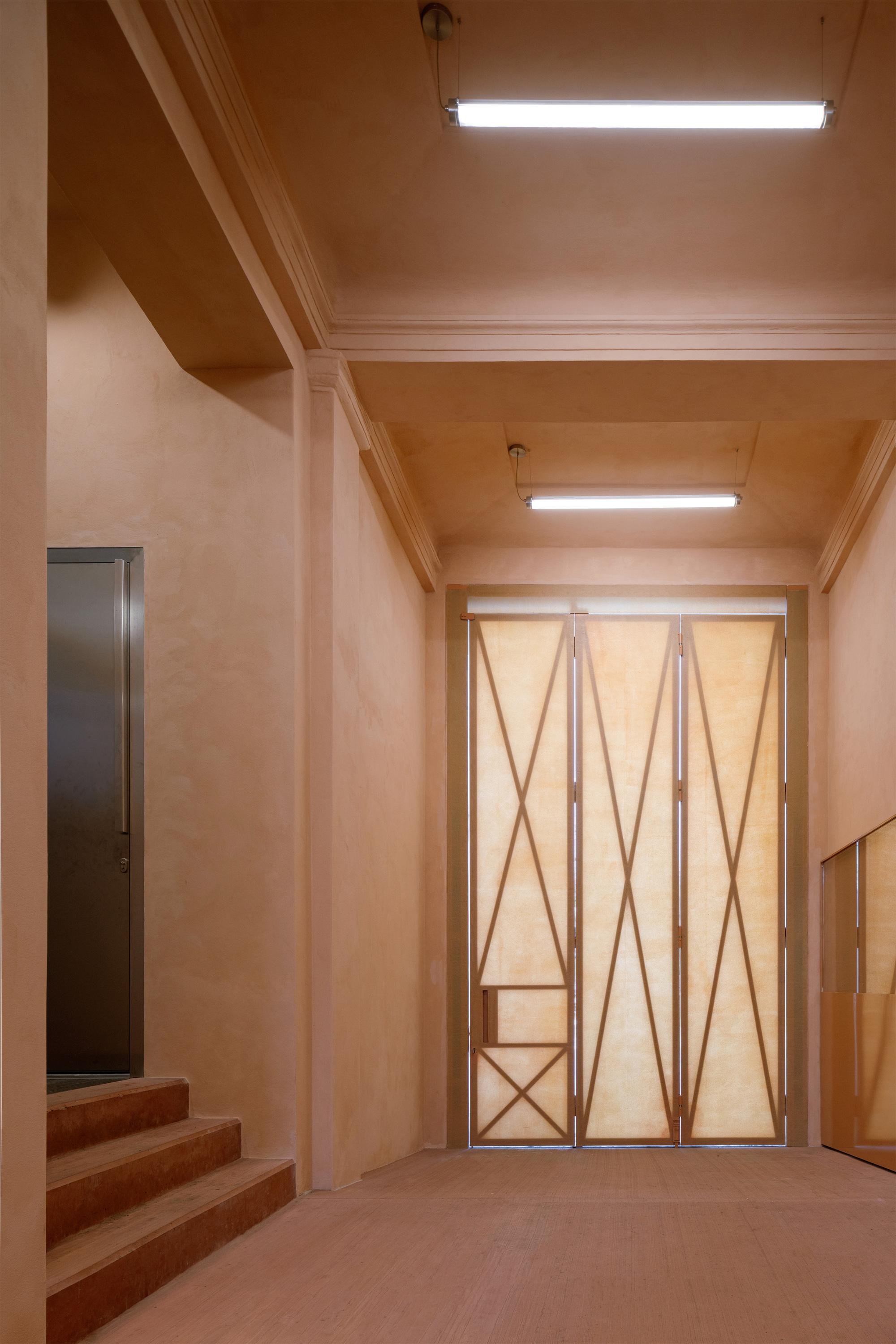Entry hall with coffered plywood ceiling and geometric folding doors under fluorescent lighting