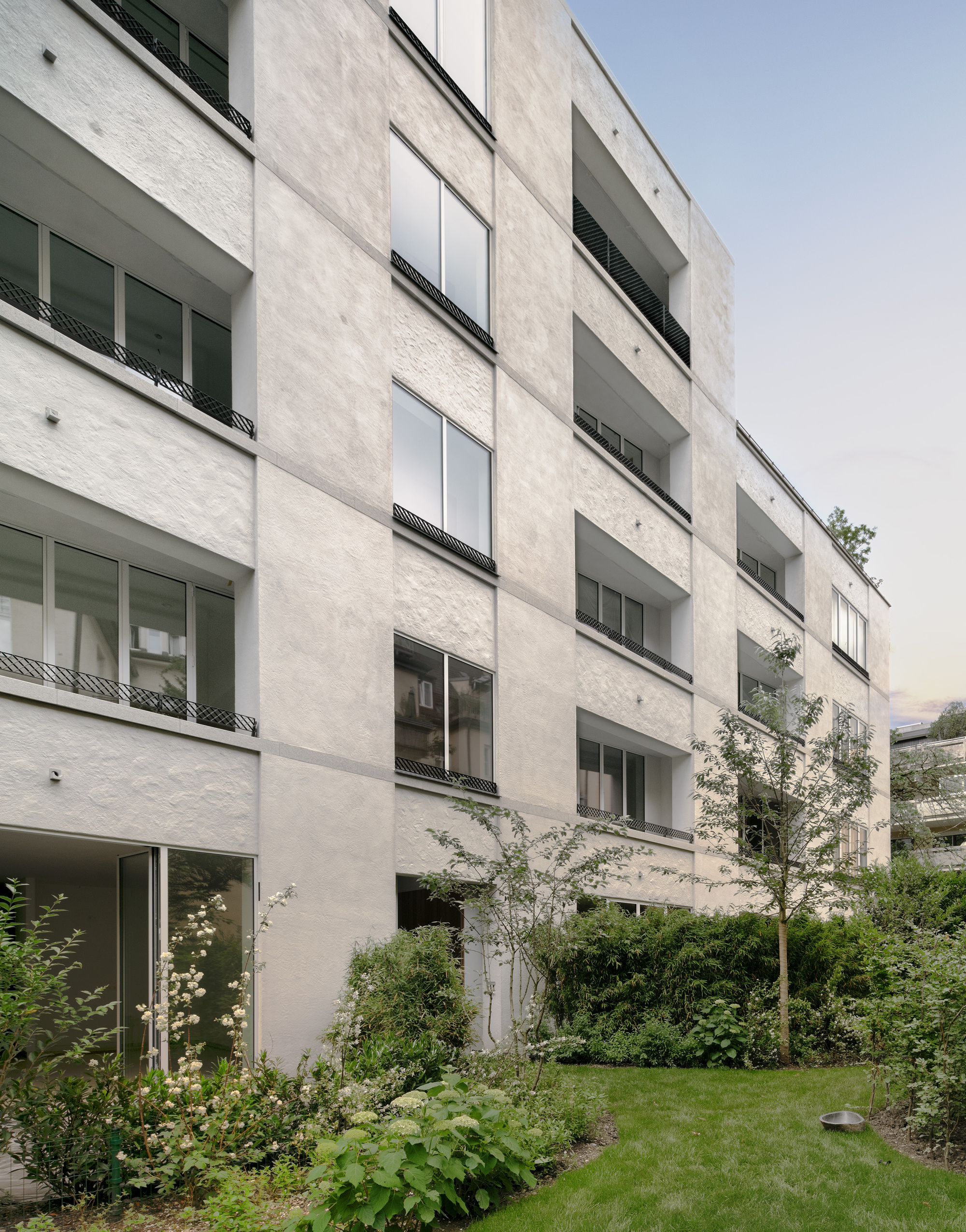 Garden view of the pale stucco facade with recessed balconies and shrubs in the foreground