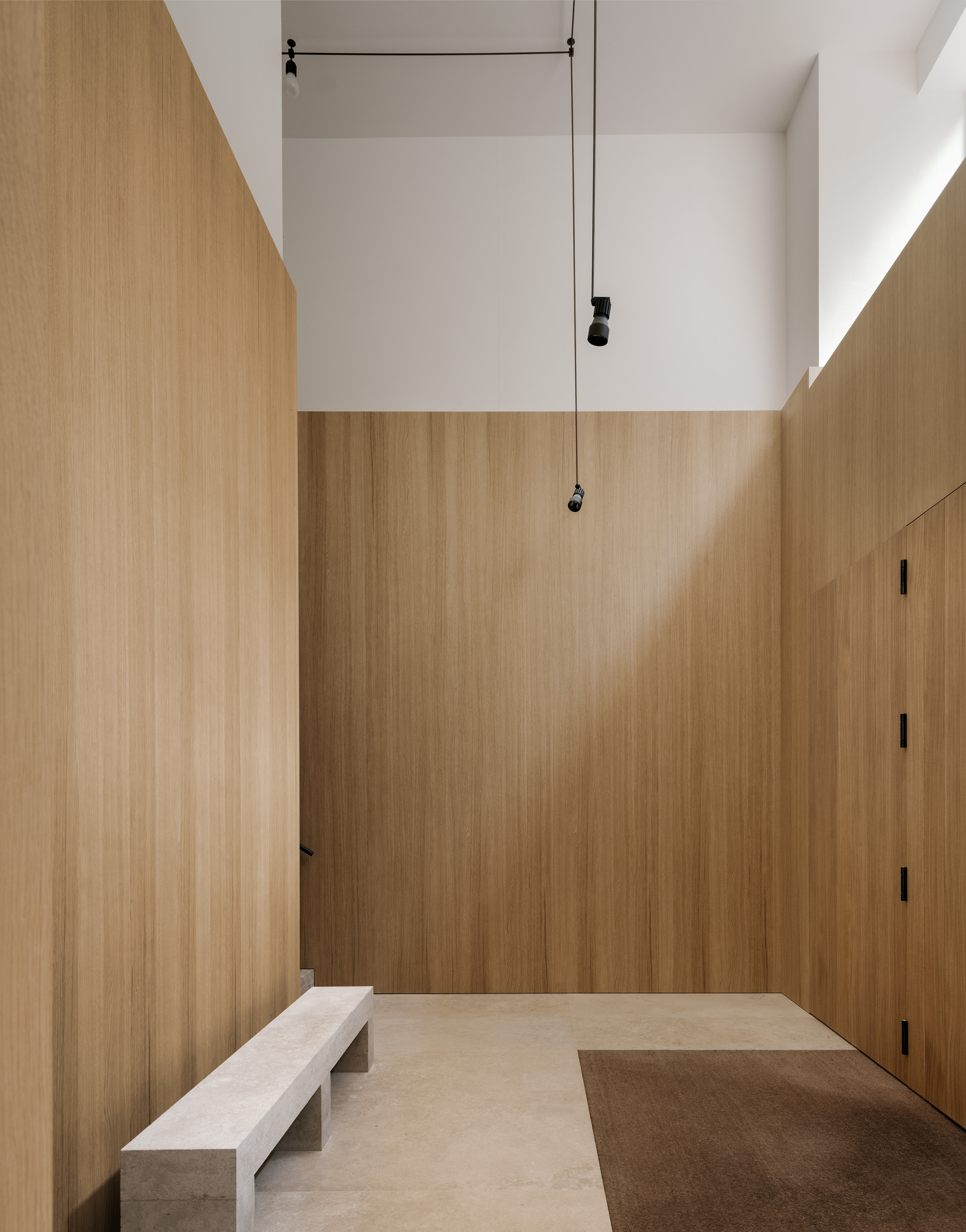 Double-height entrance hall clad in oak panels with pendant lights and stone bench seating