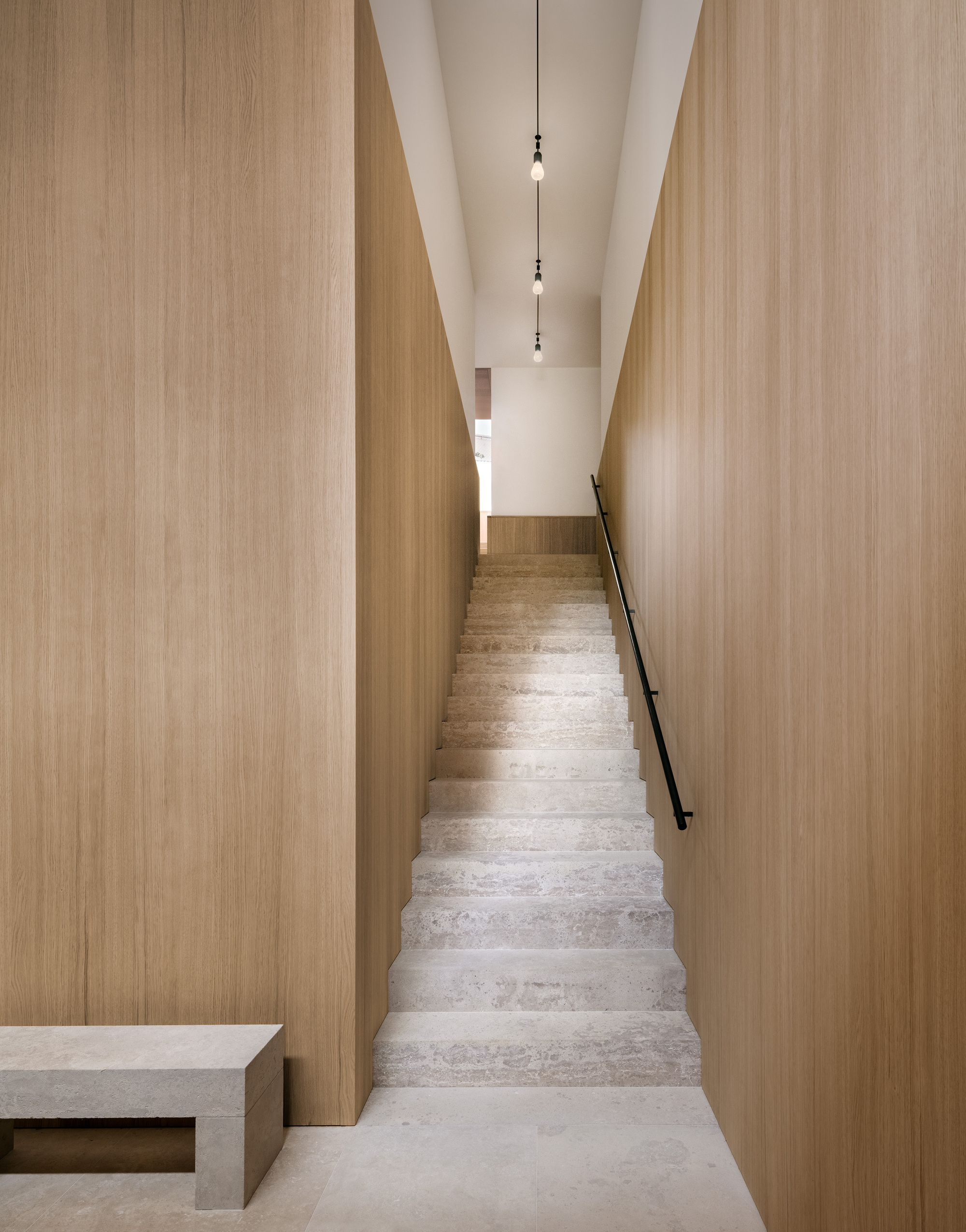 Narrow stone staircase flanked by tall timber-clad walls with pendant lights suspended from the white ceiling