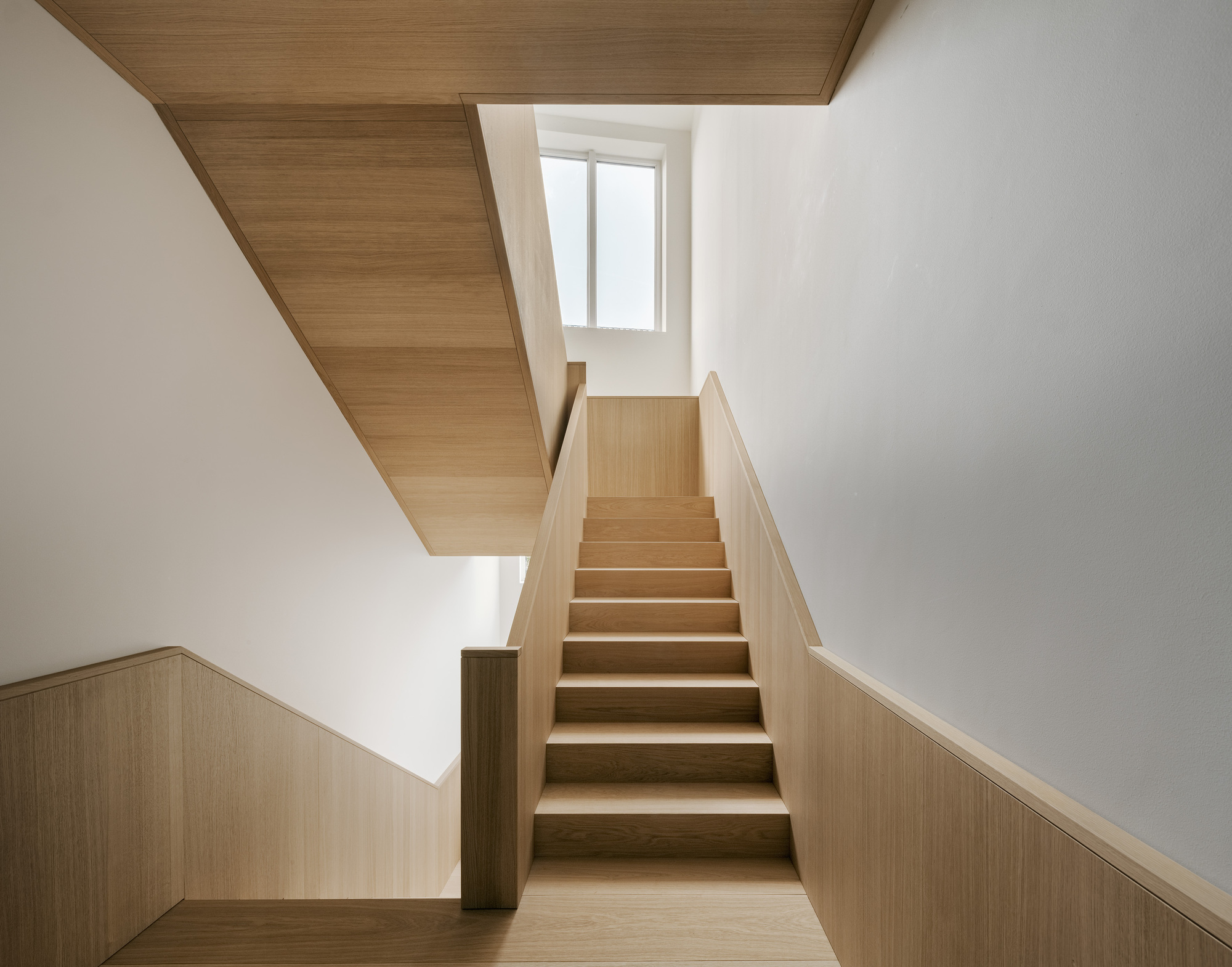 Timber staircase with wood-paneled ceiling and half-height wainscoting leading to a landing with a window