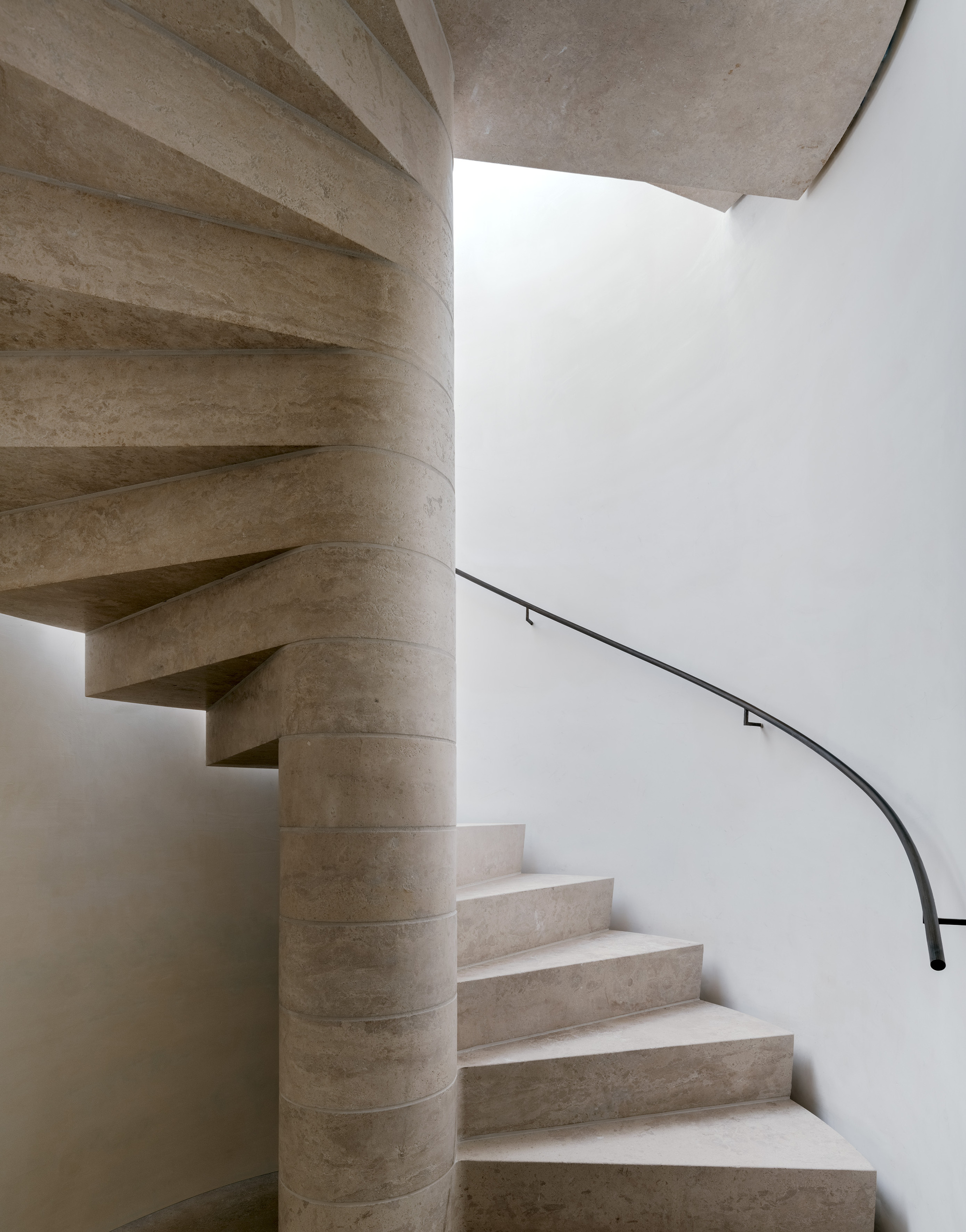 Curved stone staircase wrapping around a cylindrical core with a slender black metal handrail