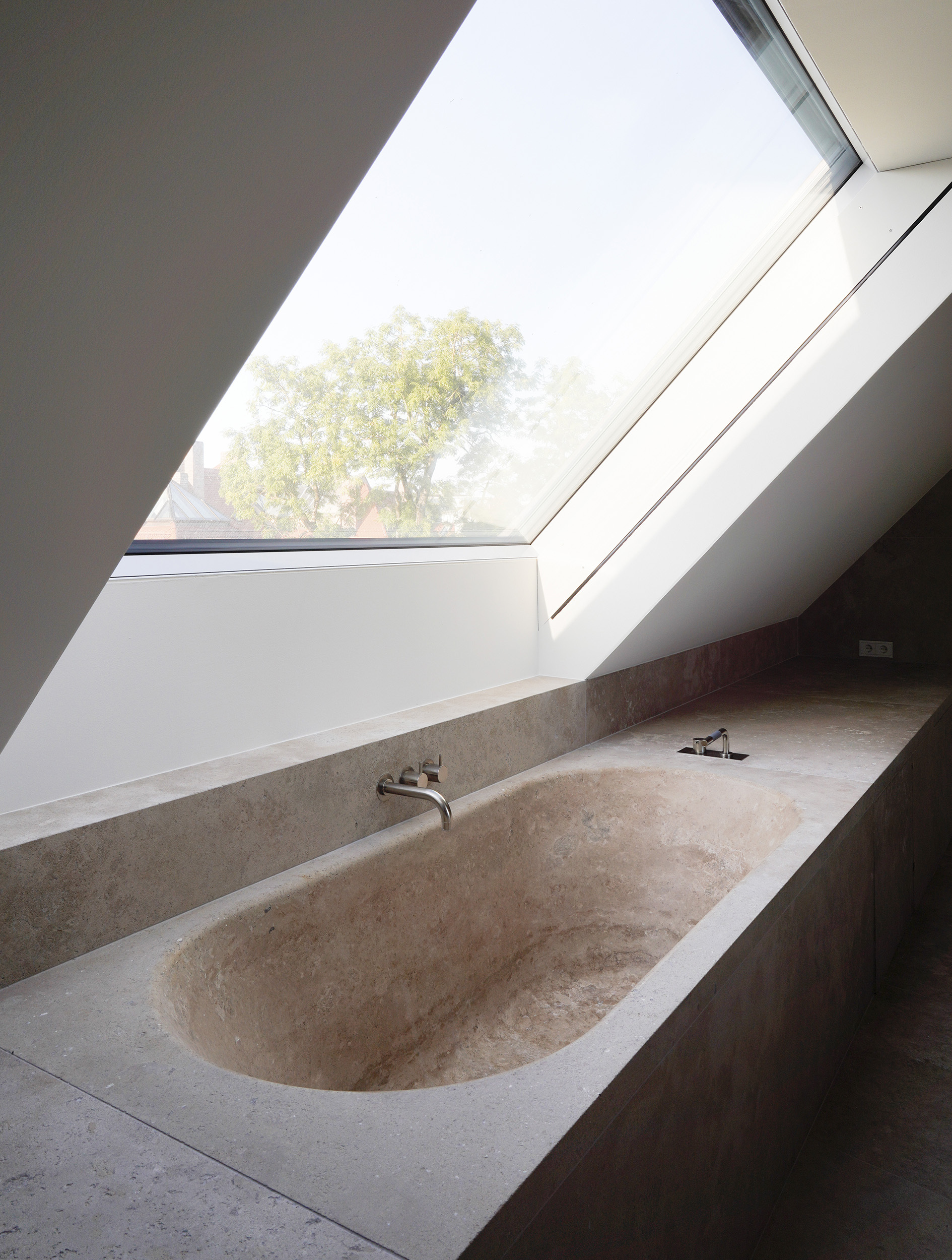 Travertine bathtub beneath an angled skylight with view to tree canopy outside