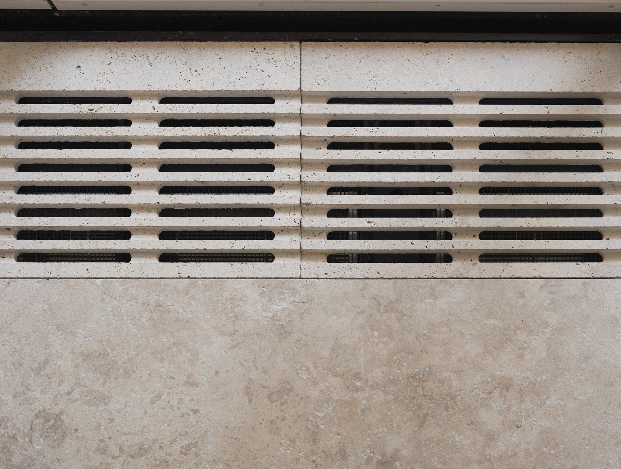 Limestone wall with horizontal black metal slat ventilation grille in four panels