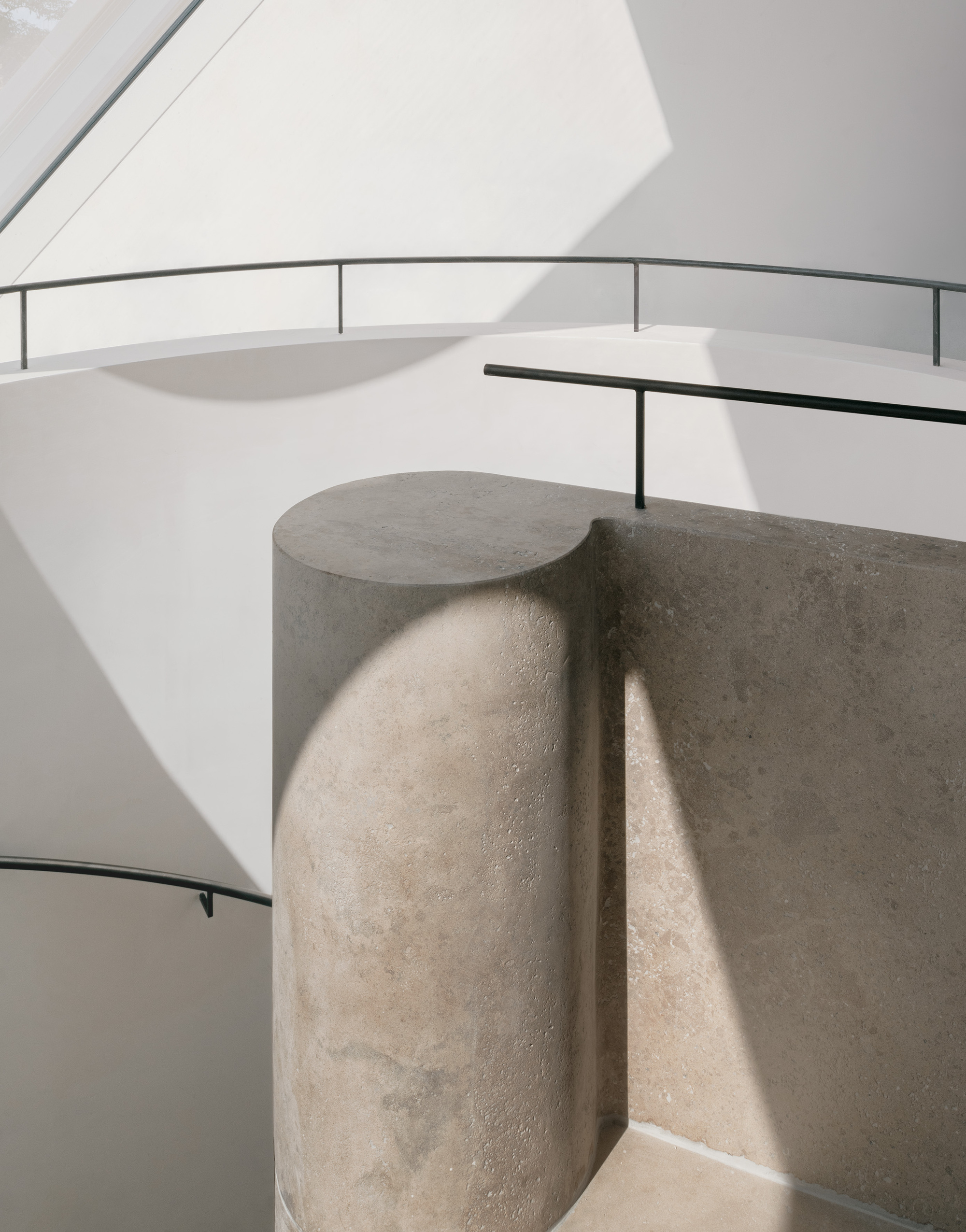 Curved stone column with cylindrical projection beside white spiral staircase with black railings
