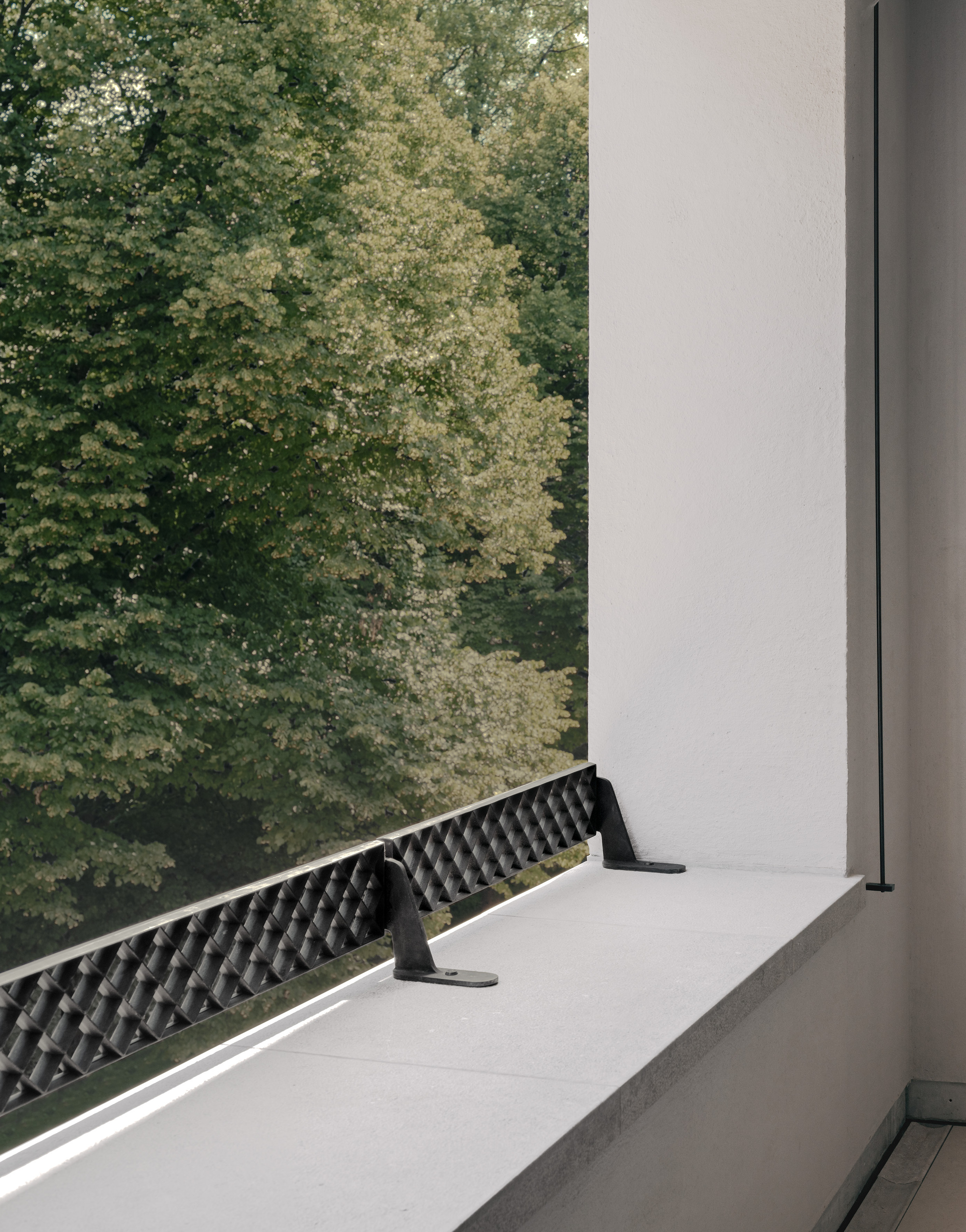 Detail of a recessed balcony with patterned metal railing and white frame overlooking green foliage