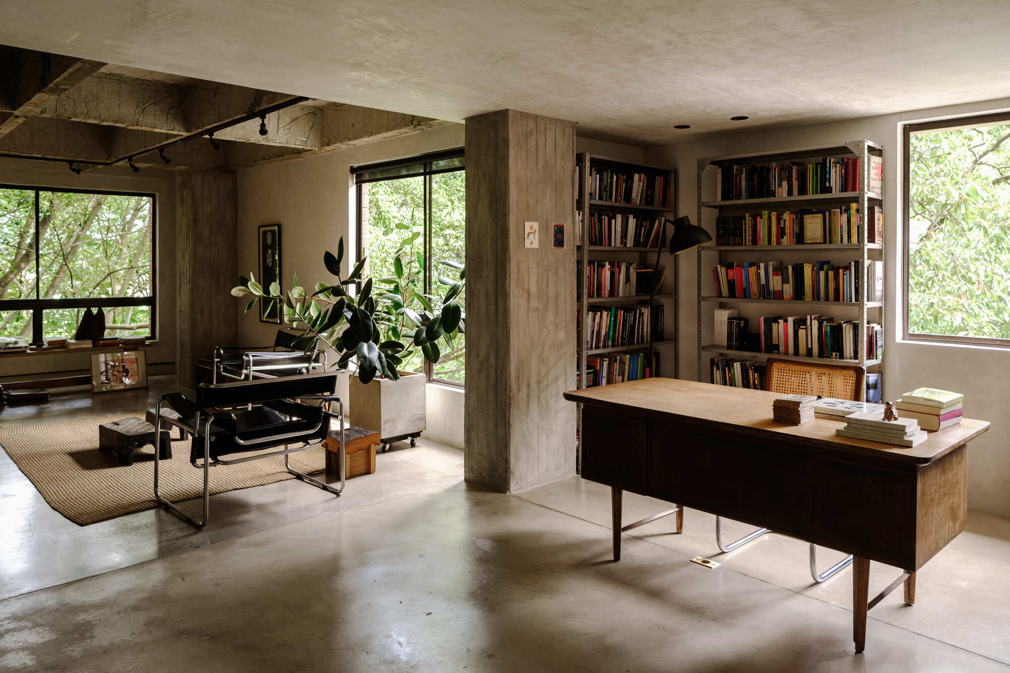 Open living area showing concrete columns, timber joinery, and floor-to-ceiling windows overlooking greenery