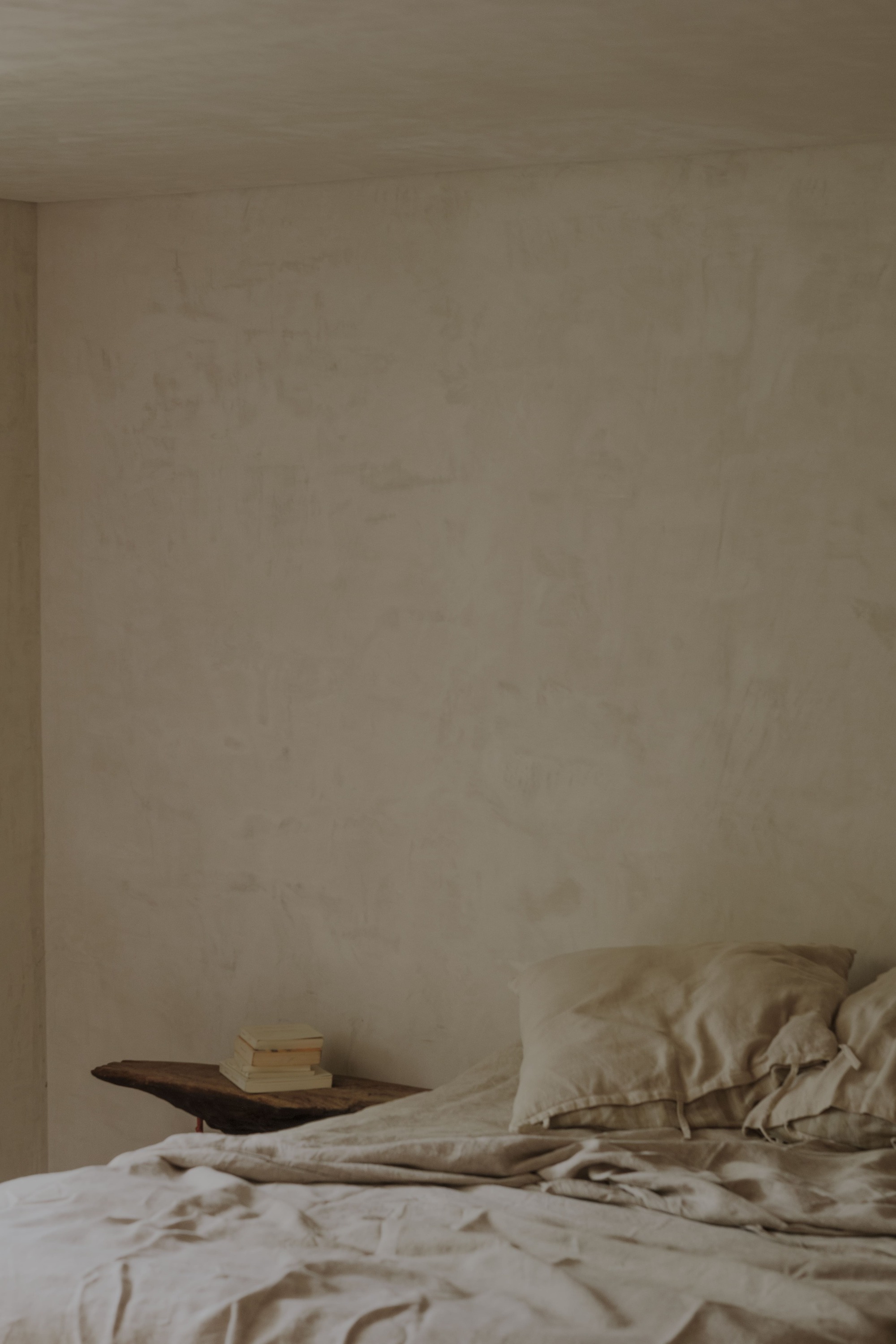 Textured plaster wall meeting the corner above a bed dressed in neutral linen