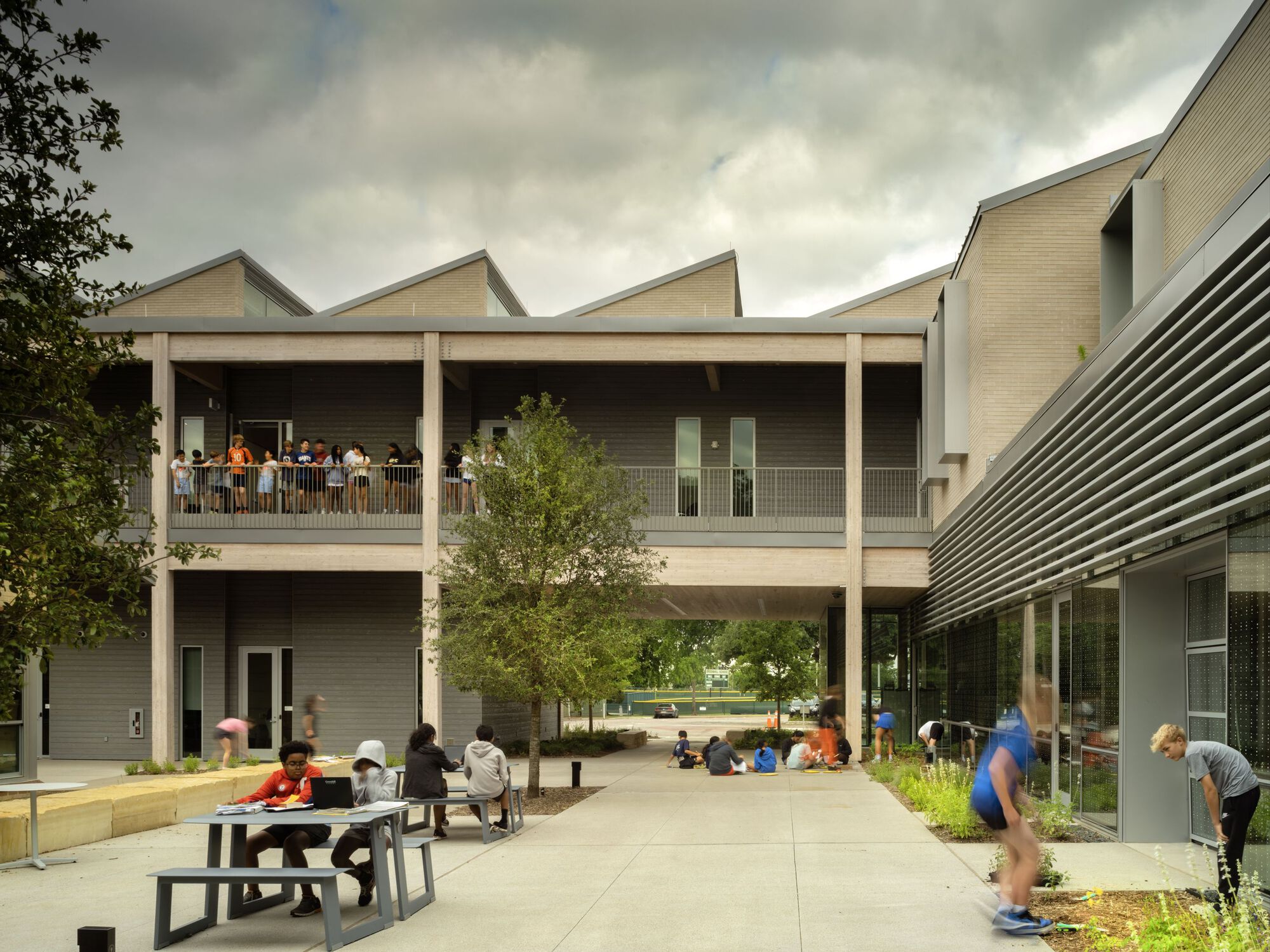 Covered outdoor courtyard with sawtooth roofline and students sitting at benches below colonnade